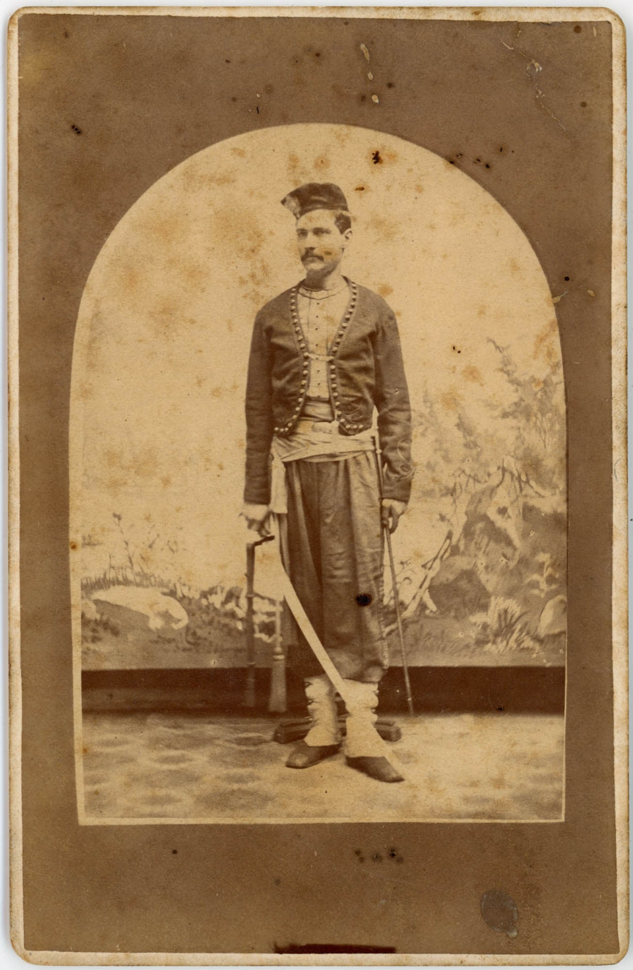 Cabinet Card, Zouave Costume with Swords, Colebaugh, PA: A man in full Zouave-style costume stands in a confident full-length pose within an arched vignette in this cabinet card by Wm. W. Colebaugh, Photographer, No. 19 Federal Street, Allegheny City, Penns