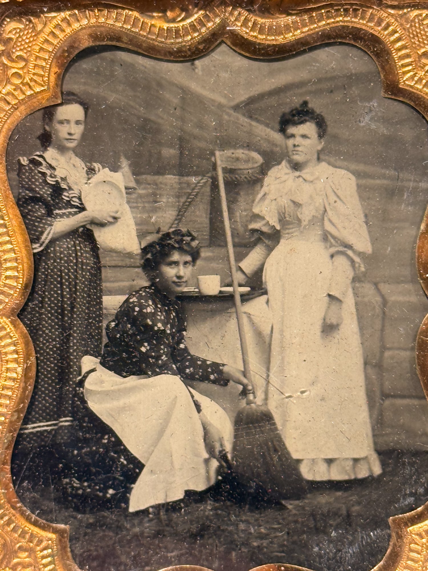 Sixth Plate Tintype, Three Maids With Broom and Household Props: Three domestic servants posed outdoors anchor this sixth plate tintype, likely made in the 1880s based on the pronounced leg-of-mutton sleeve styles visible on two of the women. All three wear dark