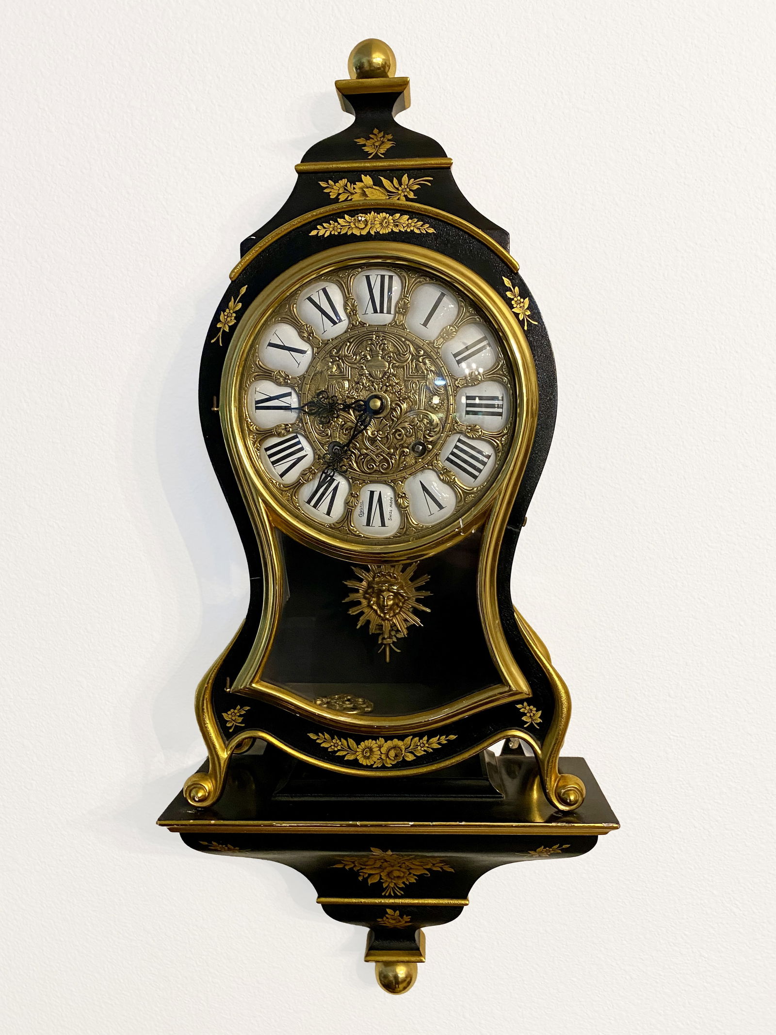 Ozura Swissmade Striking Wall Clock w/ Shelf: Ozura Swissmade striking wall clock featuring a black lacquered case with gold-tone decorative accents and floral motifs. The clock includes an ornate gilt dial with raised Roman numerals and decorati