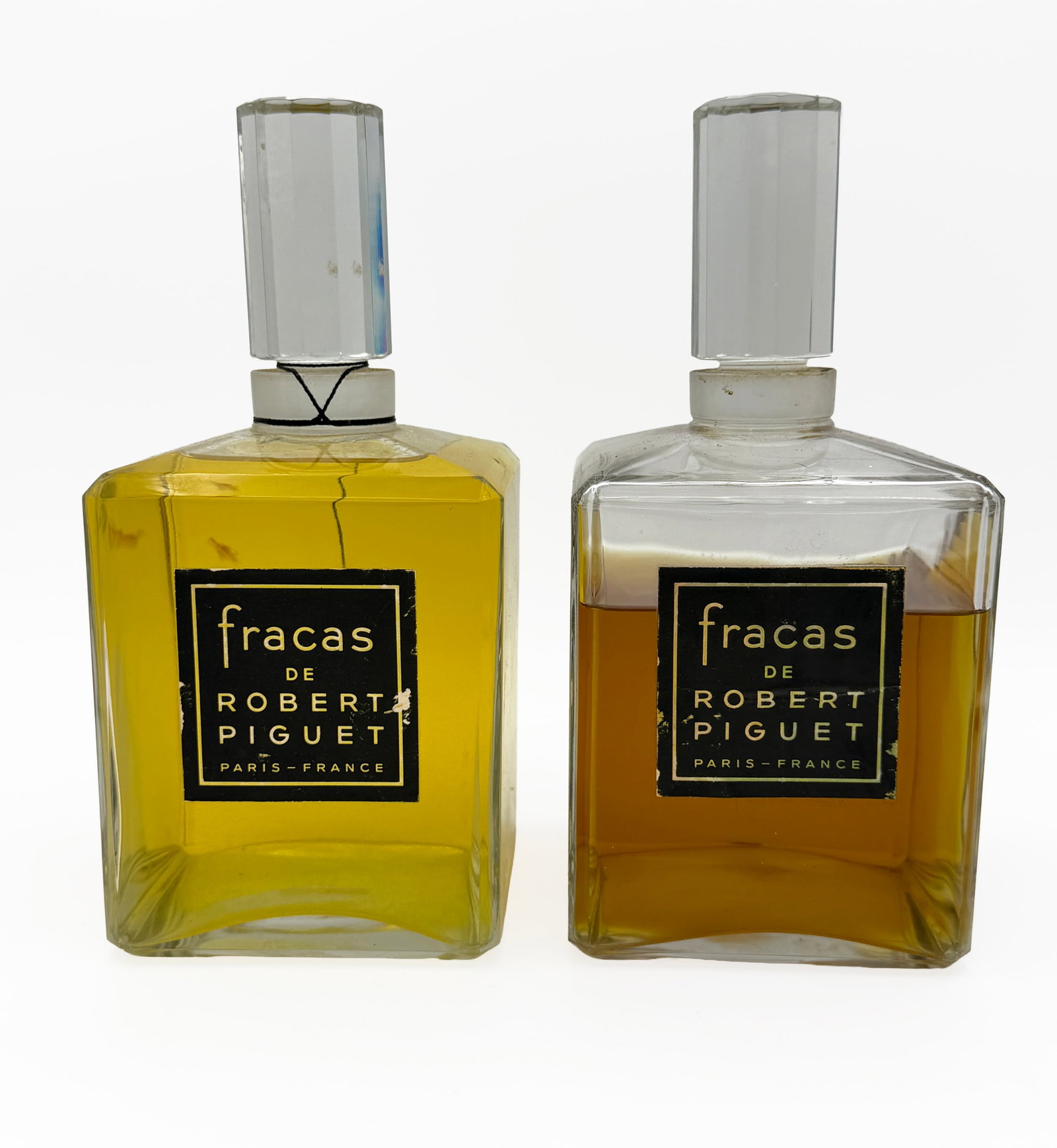 Lot of 2 Fracas de Robert Piguet Factice Perfumes: Pair of oversized Fracas de Robert Piguet French glass retail counter tester bottles, each containing Fracas perfume and fitted with a clear faceted glass stopper. Black-and-gold paper labels read “