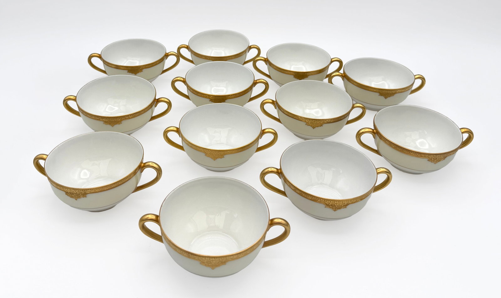 Vintage 12 Noritake Rosalie Soup Bowls: Set of 12 Noritake porcelain two-handled cream soup bowls in the Rosalie pattern, circa 1920s–1930s. Each has an ivory ground with a wide gilt border, gilt loop handles and pendant-form decoration. 