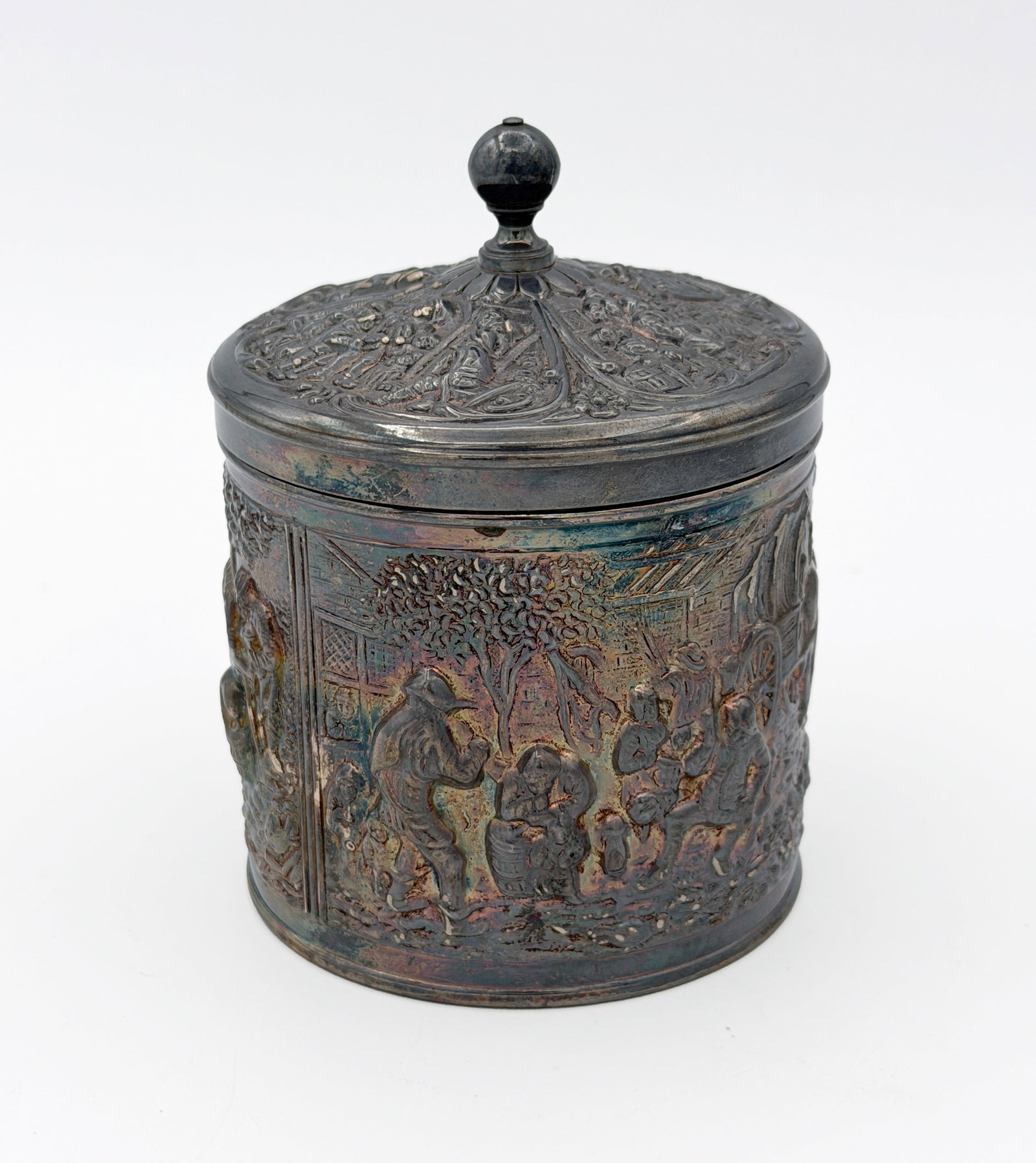 Vintage Silver Plated Dutch Tea Caddy: Vintage Dutch silver-plated tea caddy with cylindrical body and fitted lid, the exterior decorated in relief with a village scene featuring figures, buildings, and landscape elements, the lid with