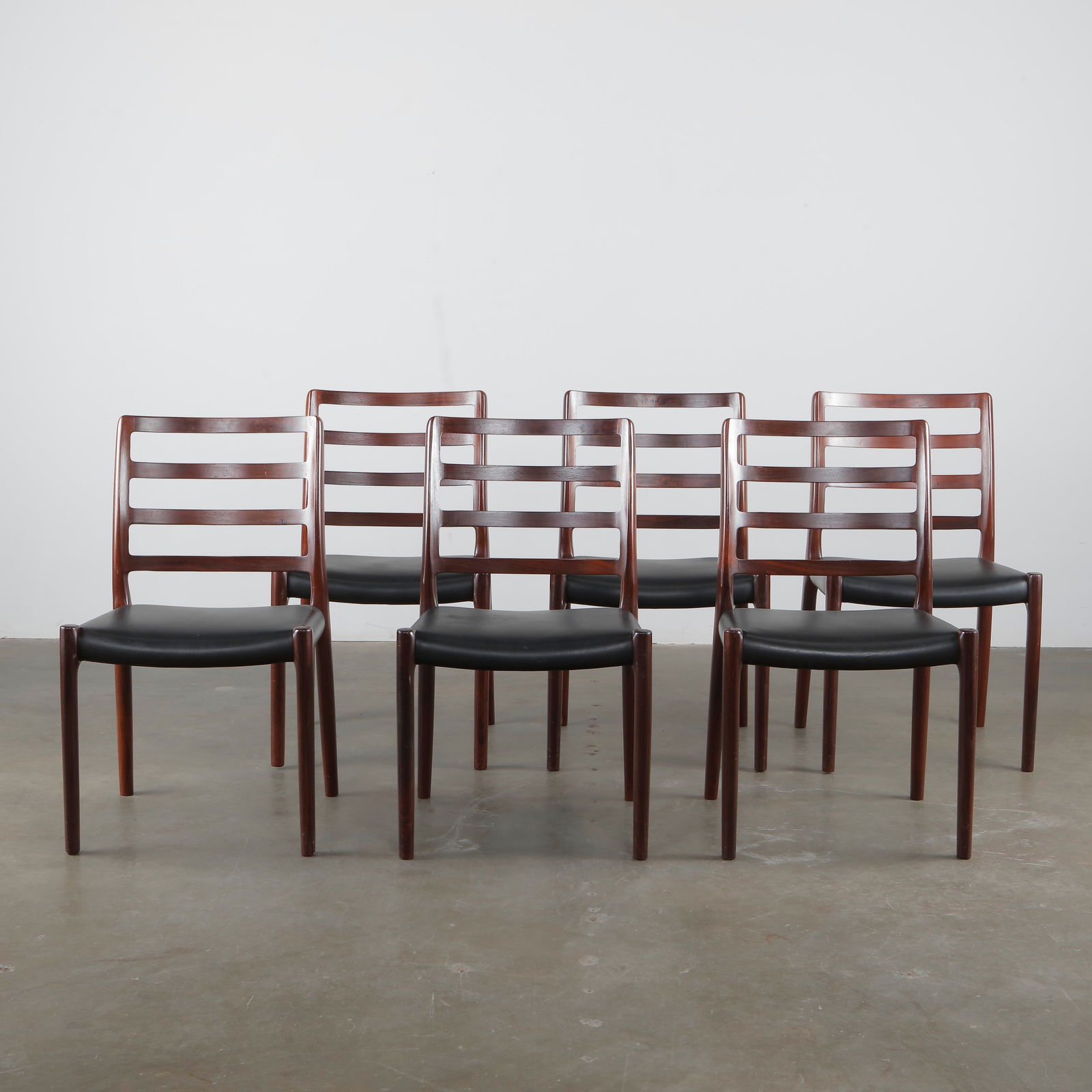 J.L. Møllers Møbelfabrik , Set of Six Black Leather and Wood Dining Chairs, 1970s: Elegant set of six dining chairs by J.L. Møllers Møbelfabrik, featuring sculpted teak frames and black leather seats. Denmark, 1960s. Height: 35 in. Width: 20 in. Depth: 17 in. Seat Height: 17 in.