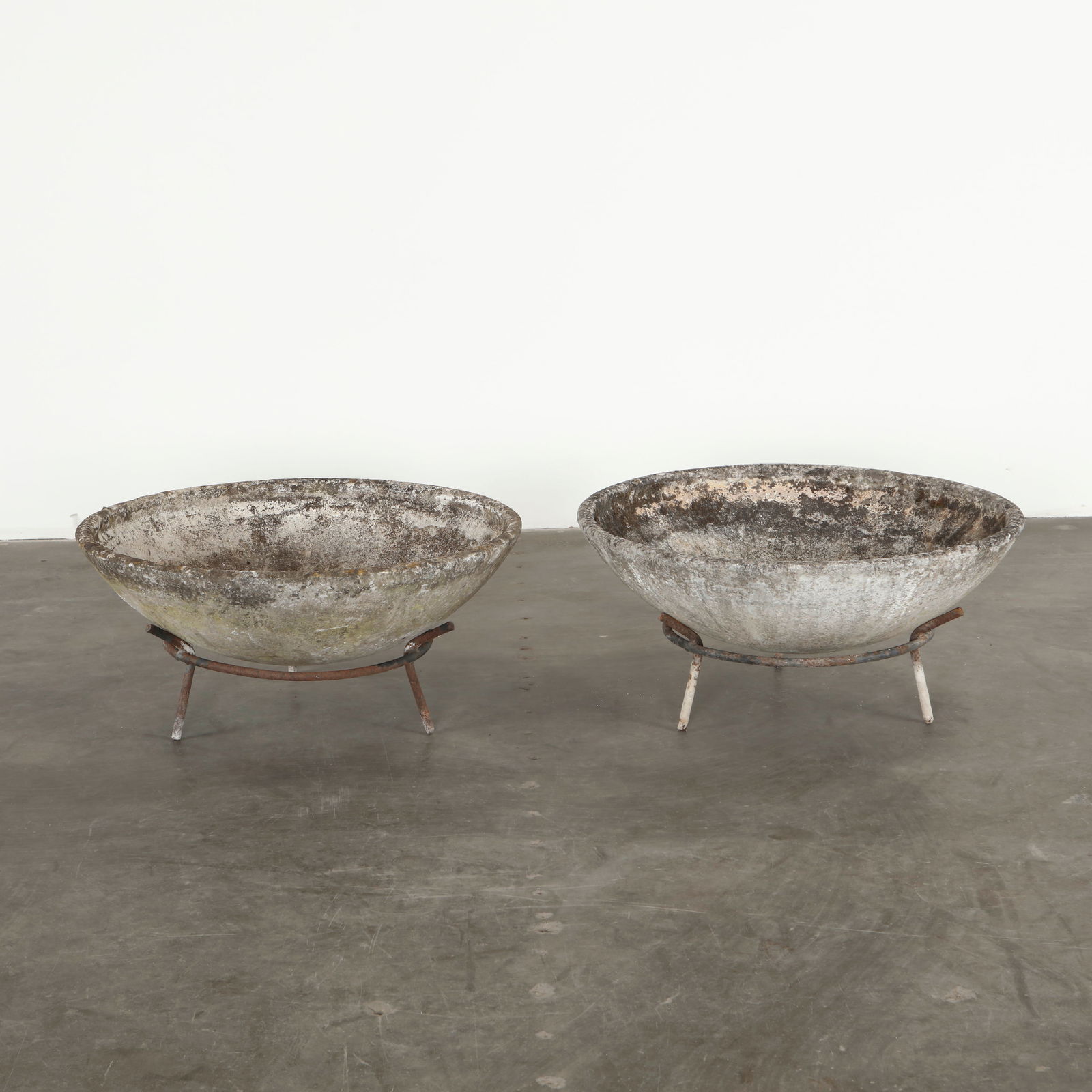Willy Guhl, Pair of Bowl Planters on Stands, 1960s: Each planter presents a shallow circular bowl in concrete resting on metal legs. Designed by Willy Guhl, these pieces exemplify his sculptural approach to functional outdoor forms. Their weathered sur