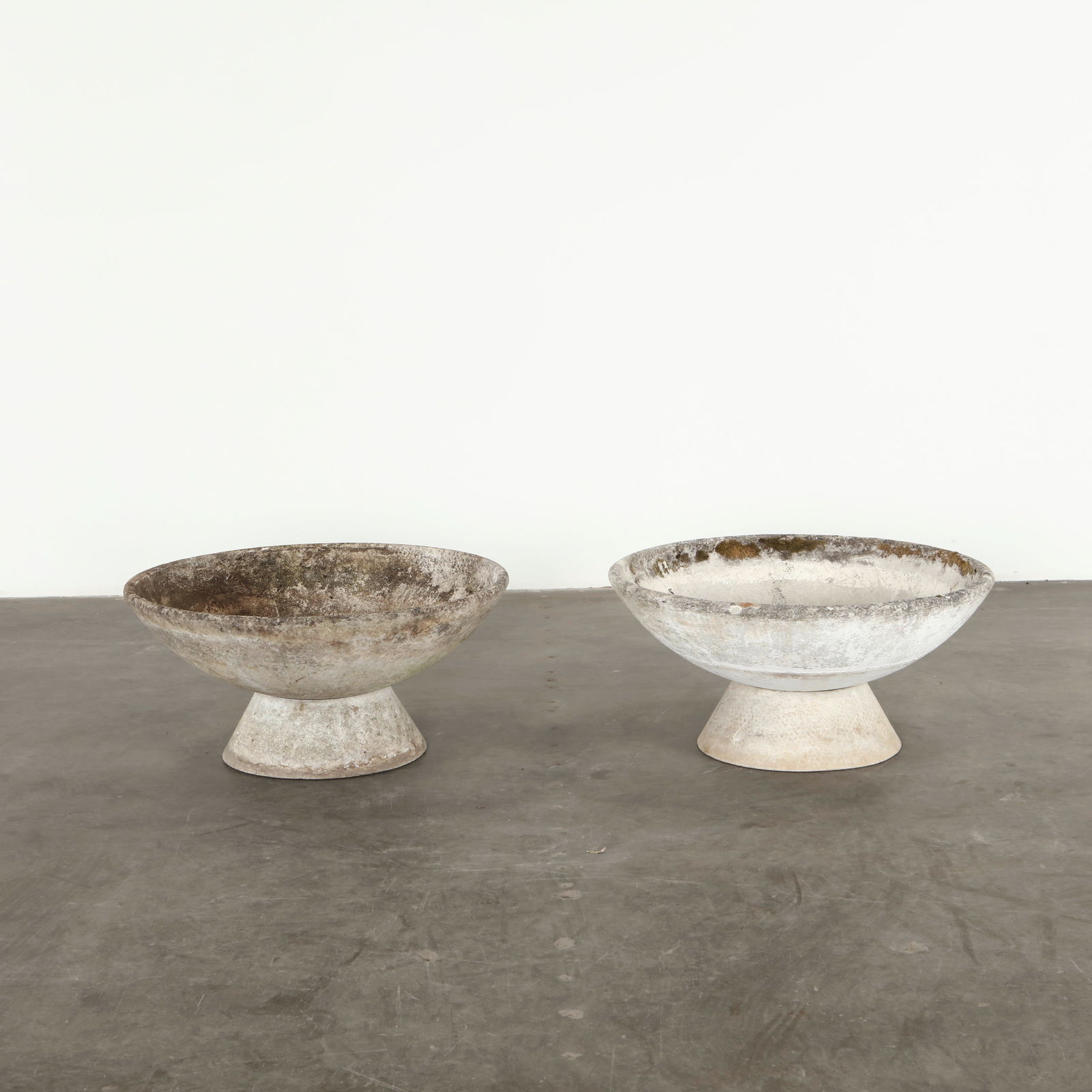 Willy Guhl, Pair of Bowl Planters on Stands, 1960s: Each planter presents a shallow circular bowl in concrete resting on a concrete stand. Designed by Willy Guhl, these pieces exemplify his sculptural approach to functional outdoor forms. Their weather