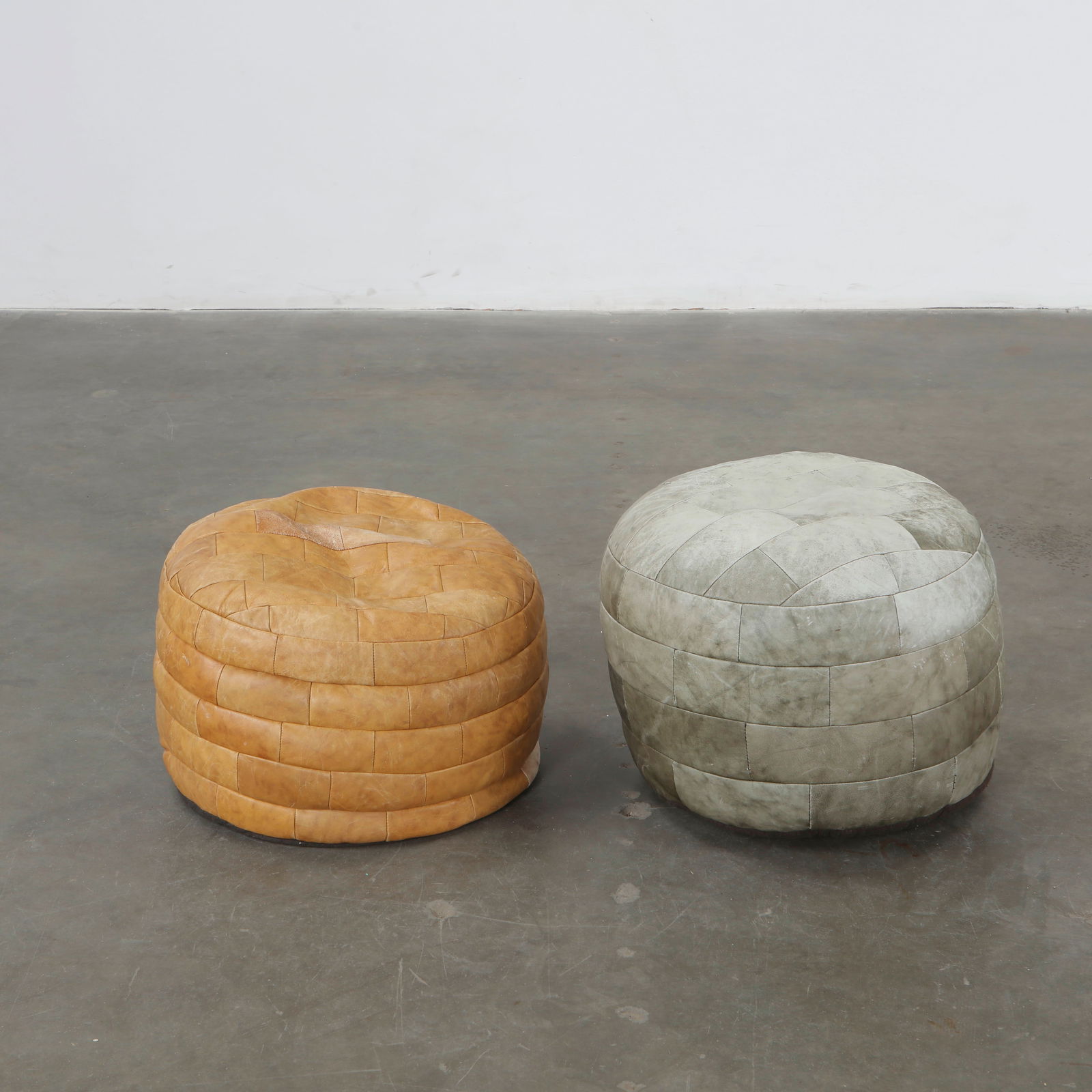 De Sede, Set of Two Leather Ottomans, 1960s: Vintage De Sede leather poufs in beige and gray tones. Swiss design, superb patina. Beige: Height: 11.5 in. Diameter: 20 in. Grey: Height: 17 in. Diameter: 20 in.