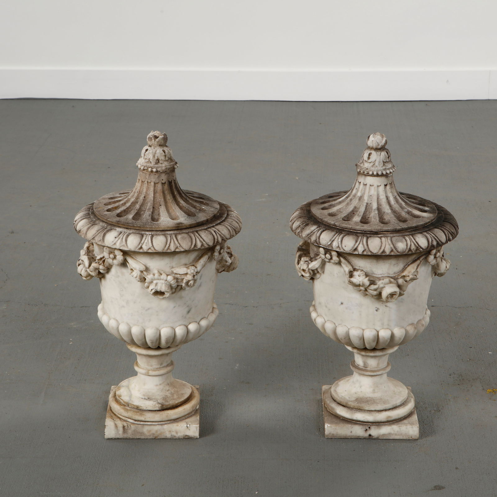 Carrara Marble Castle Sculpture, France, 17th Century: Pair of carved Carrara marble urns with integral domed tops, featuring classical baluster forms, floral garlands and bead molding. Provenance from a French castle, with a richly weathered patina