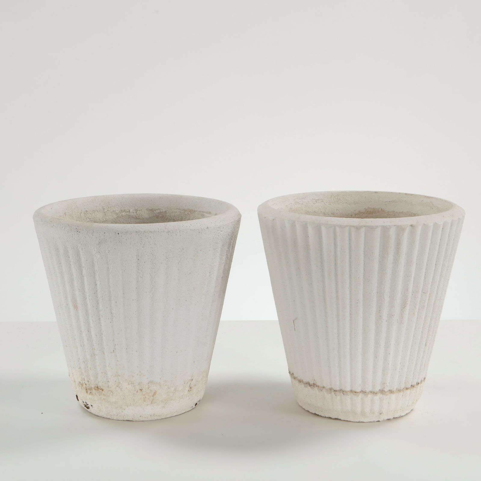Pair of White Stone Planters, 1960s: Executed in cast stone with a vertically fluted profile, these planters feature a clean tapering silhouette softened by a naturally weathered patina. A restrained and architectural pair, evocative of