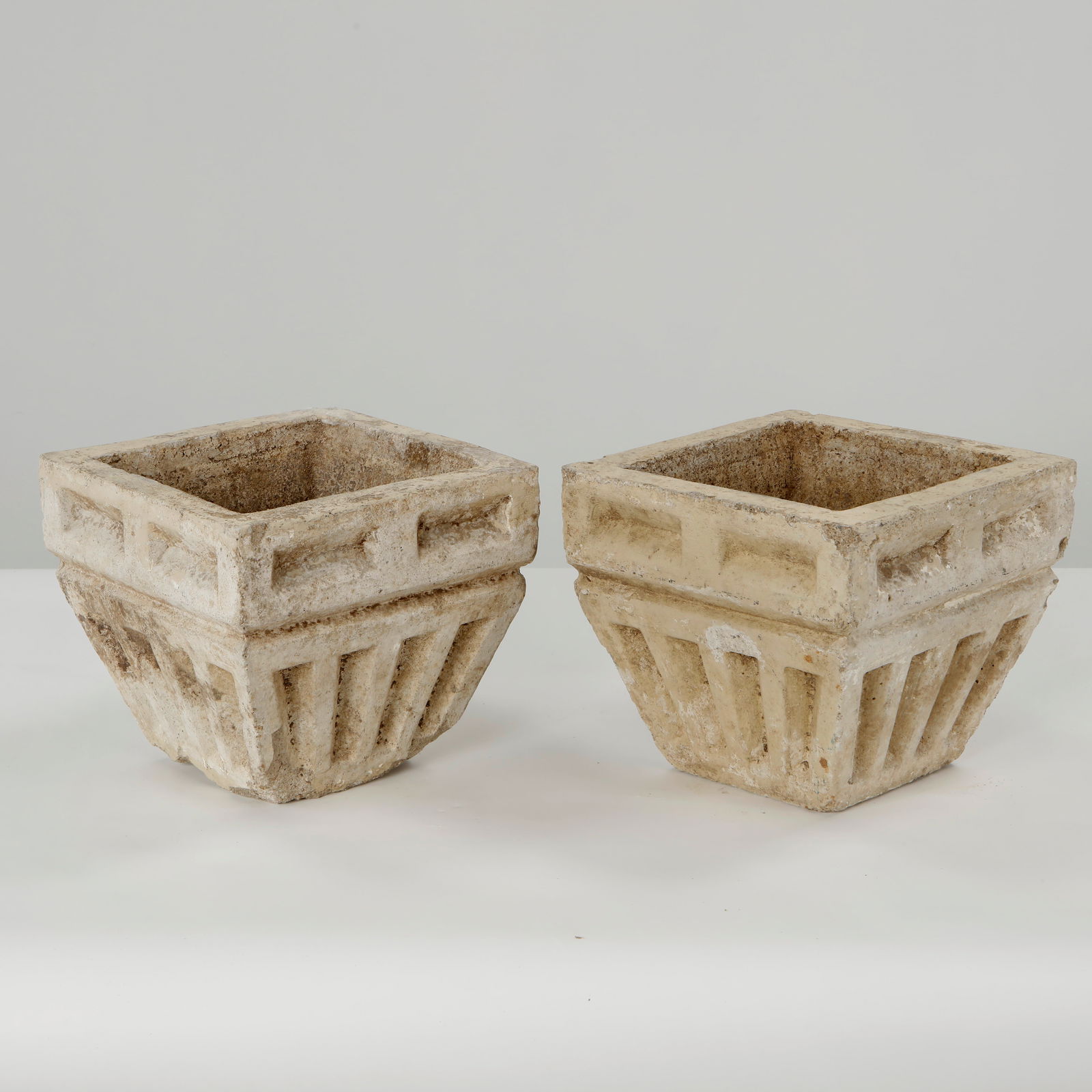Pair of Architectural Square Relief Stone Planters, 1950s: Square stone planters with recessed architectural detailing and stepped bases, exhibiting strong relief work and a richly weathered garden patina. Height: 8.5 in. Length: 9.5 in. Depth: 9.5 in.