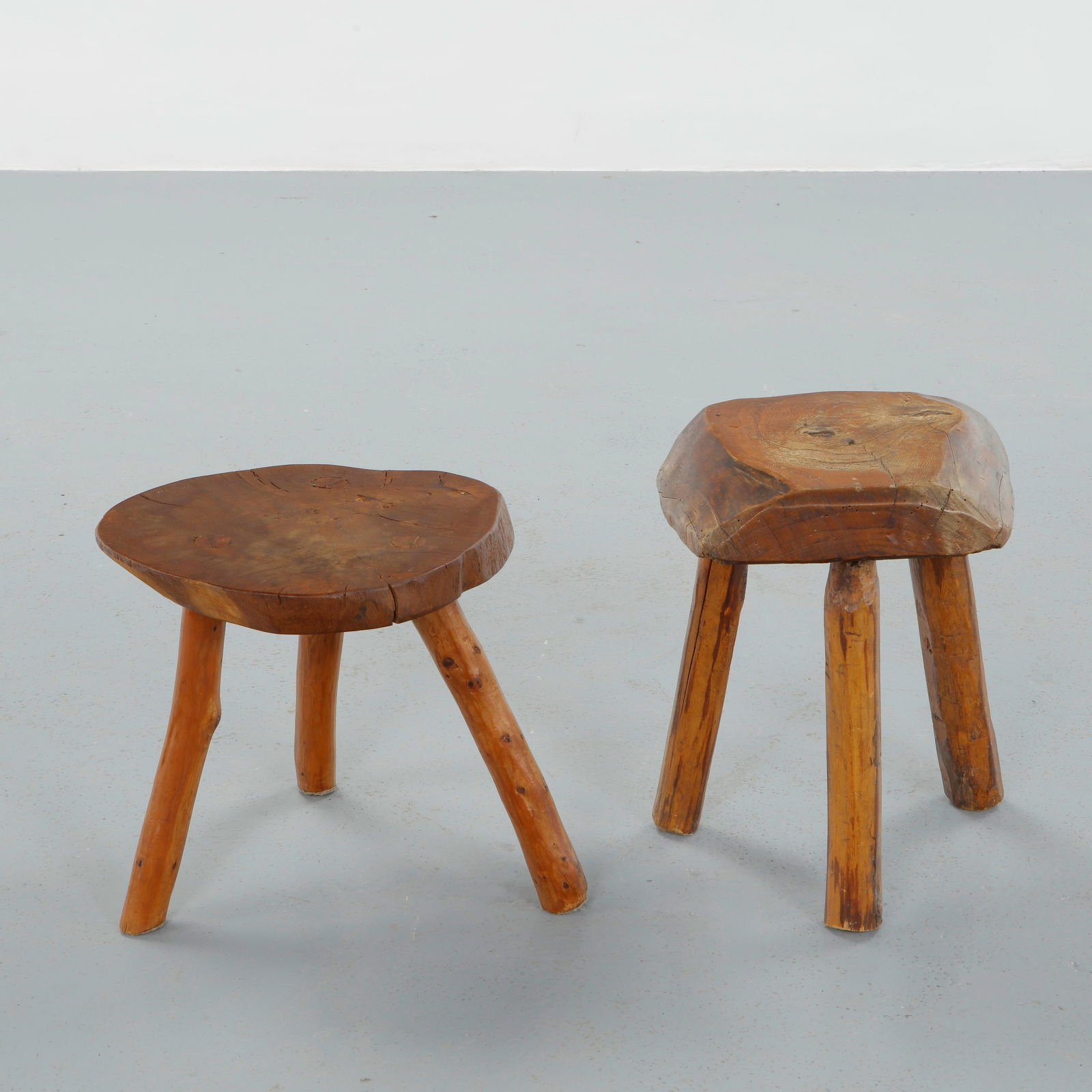French Provincial, Pair of Sculpted Wood Tripod Stools, 1950s: Executed in solid hardwood with gently faceted seats and splayed cylindrical legs, this pair reflects utilitarian origins elevated by sculptural presence. The visible growth rings and hand finished su
