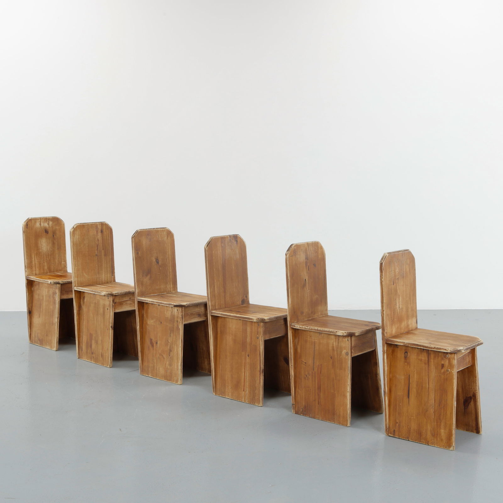 Set of Six French Provincial Chairs, 1960s: Executed in solid pine, this suite of six chairs features tall plank backs and recessed panel supports, reflecting the restrained vernacular language of rural French craftsmanship. The softly worn