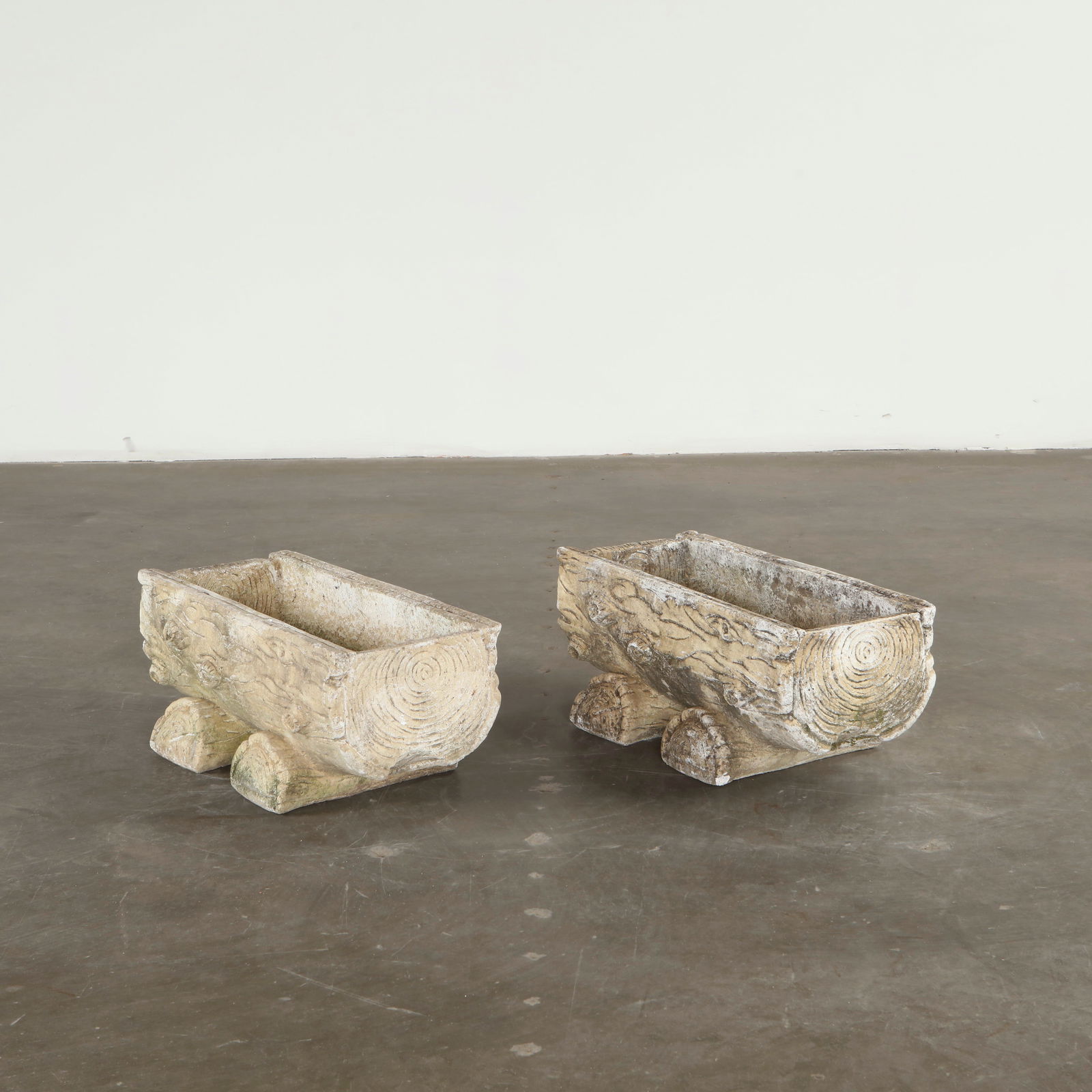 Pair of Faux Bois Trunk Planters, 1960s: Cast in stone with richly modeled faux bois textures, these rectangular planters emulate carved tree trunks resting on rounded supports. The intricate surface detailing and weathered patina reflect th