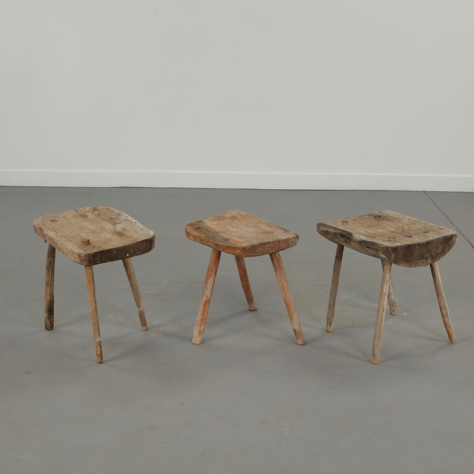 Set of Three Primitive Farmhouse Stools, 1960s: A set of three primitive farmhouse stools crafted from solid wood with expressive hand worked surfaces. Each piece emphasizes raw materiality and functional sculptural presence. 1: Height: 18.5 in. Le