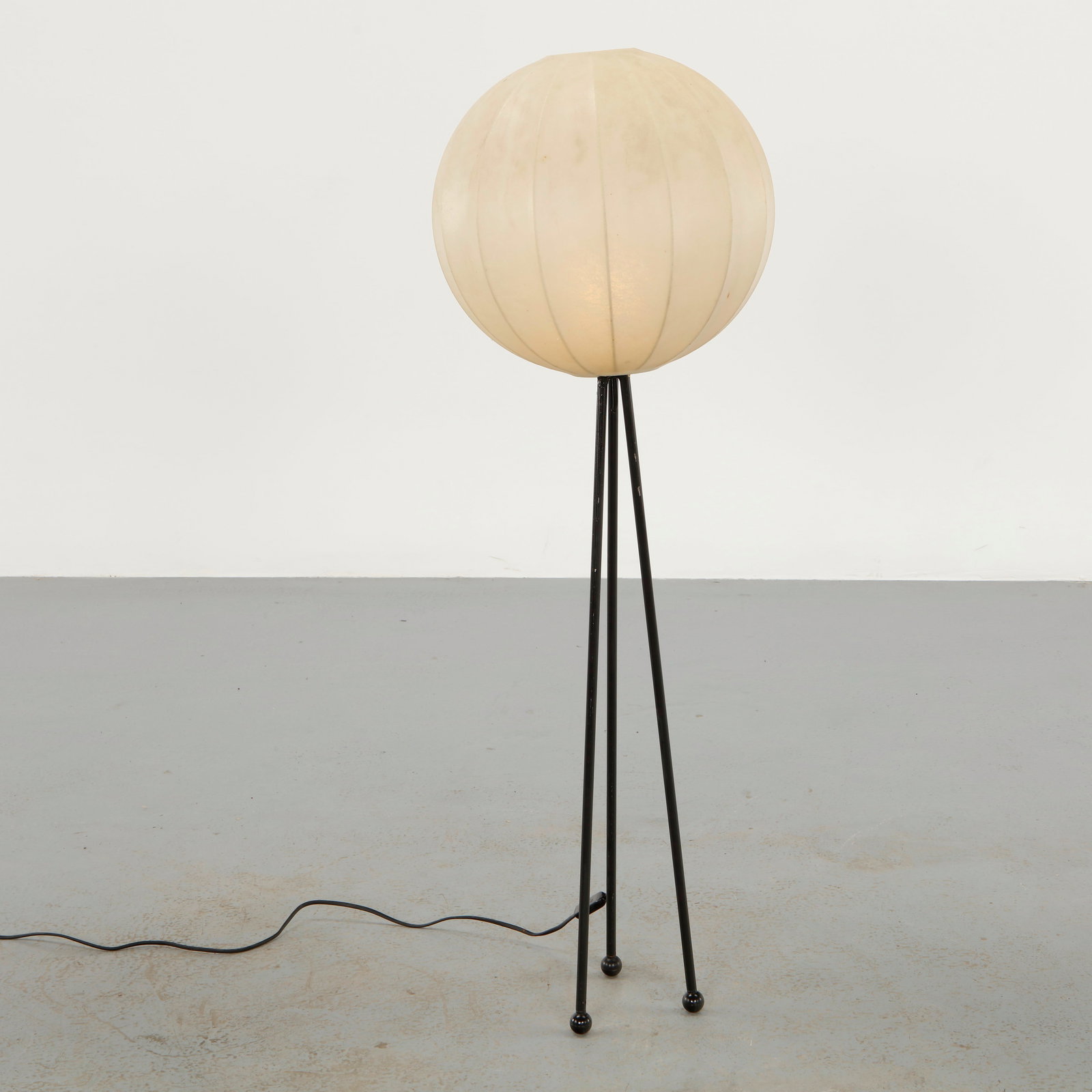 Mid-Century Tripod Cocoon Floor Lamp attributed to Goldkant Leuchten, 1950s: Raised on slender black metal tripod legs, the lamp supports a spherical shade executed in stretched parchment skin over a metal frame. The warm translucent surface diffuses light softly, emphasizing