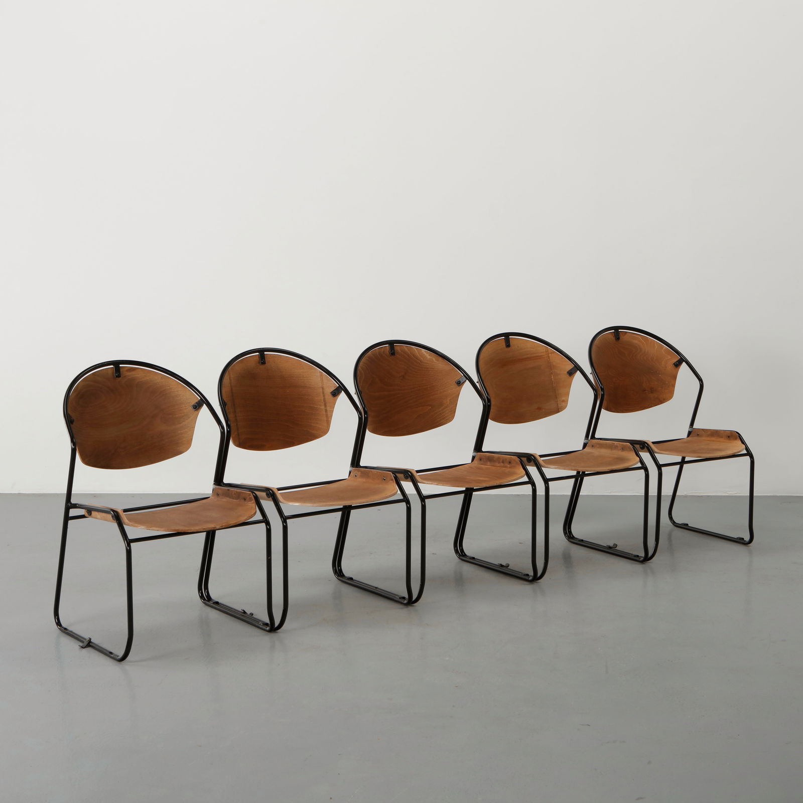 Set of Five Stacking Chairs in the style of Bruce Gueswel, 1960s: Executed with curved plywood back and seat mounted on a tubular steel frame designed for efficient stacking. The flowing lines of the shell contrast with the architectural clarity of the metal