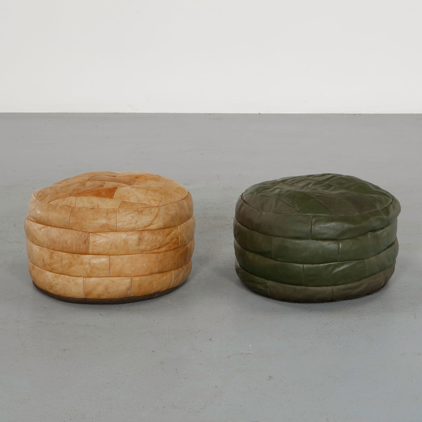 De Sede, Pair of Leather Ottomans, 1960s: Executed in hand-stitched patchwork leather, these sculptural ottomans exemplify De Sede signature craftsmanship and supple upholstery. Their green and beige tones and generous forms invite both comfo
