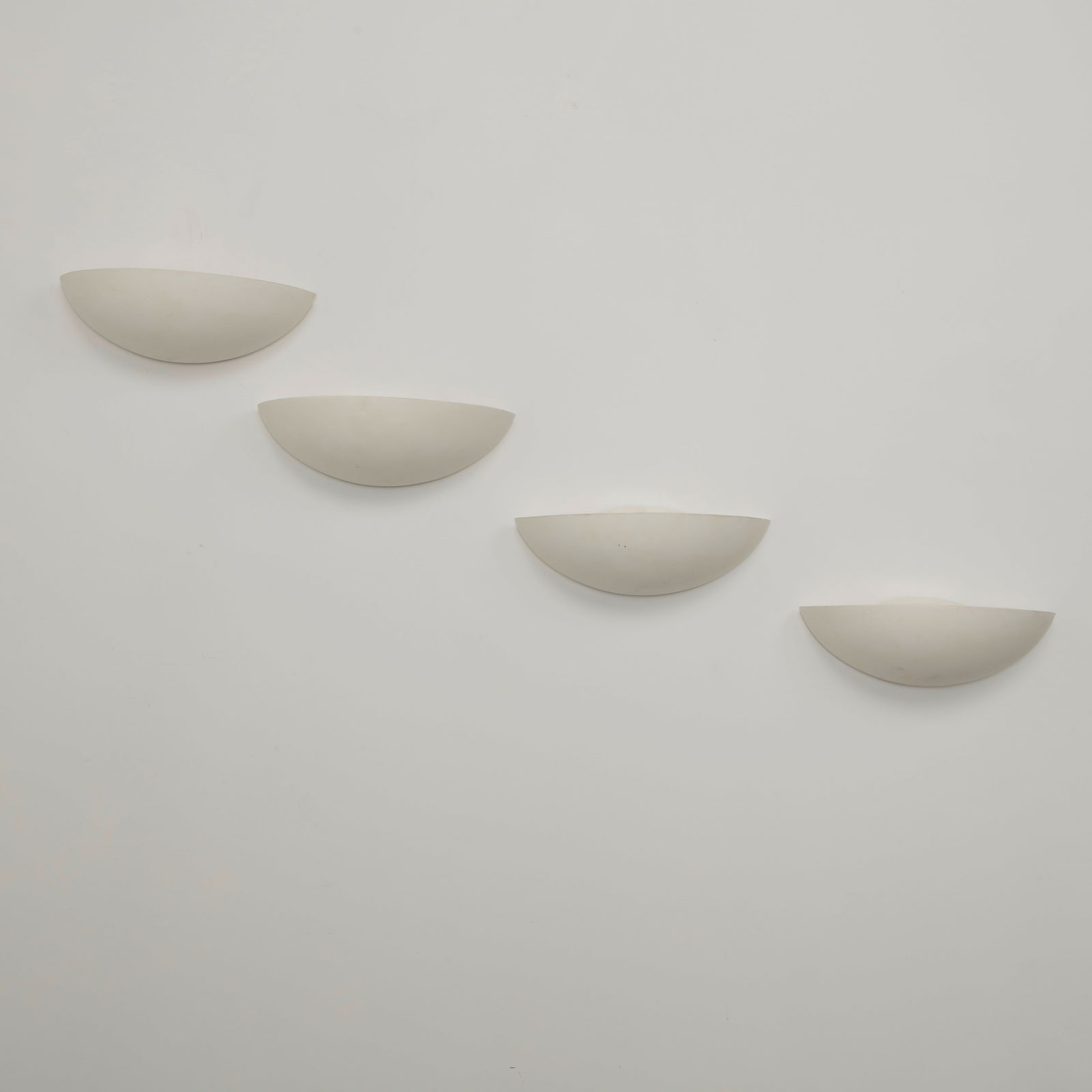 SCE, Set of Four Ceramic Wall Sconces, 1980s: Elegant half moon wall sconces executed in white ceramic with softly curved profiles that diffuse light upward and outward. Their restrained geometric form reflects the clean architectural language of