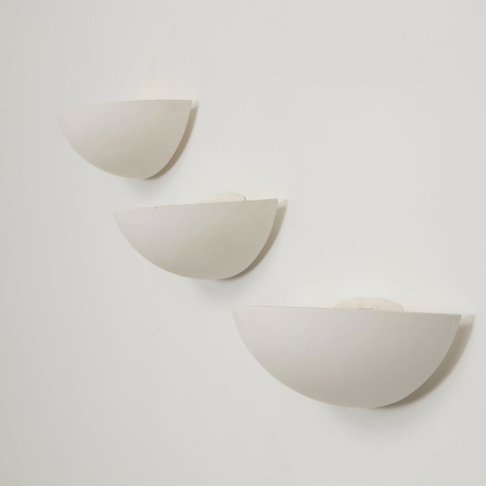 SCE, Set of Three Ceramic Wall Sconces, 1980s: Elegant half moon wall sconces executed in white ceramic with softly curved profiles that diffuse light upward and outward. Their restrained geometric form reflects the clean architectural language of
