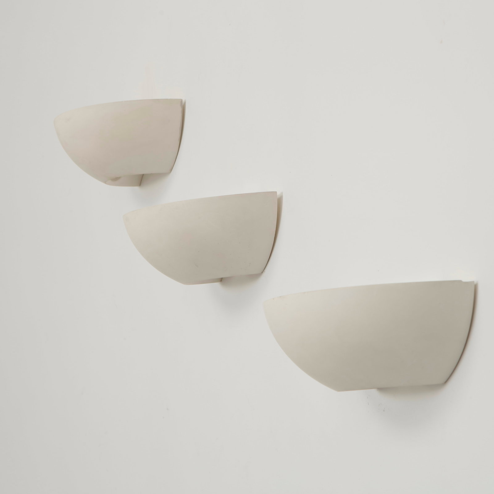 SCE, Set of Three Ceramic Wall Sconces, 1980s: Elegant half moon wall sconces executed in white ceramic with softly curved profiles that diffuse light upward and outward. Their restrained geometric form reflects the clean architectural language of