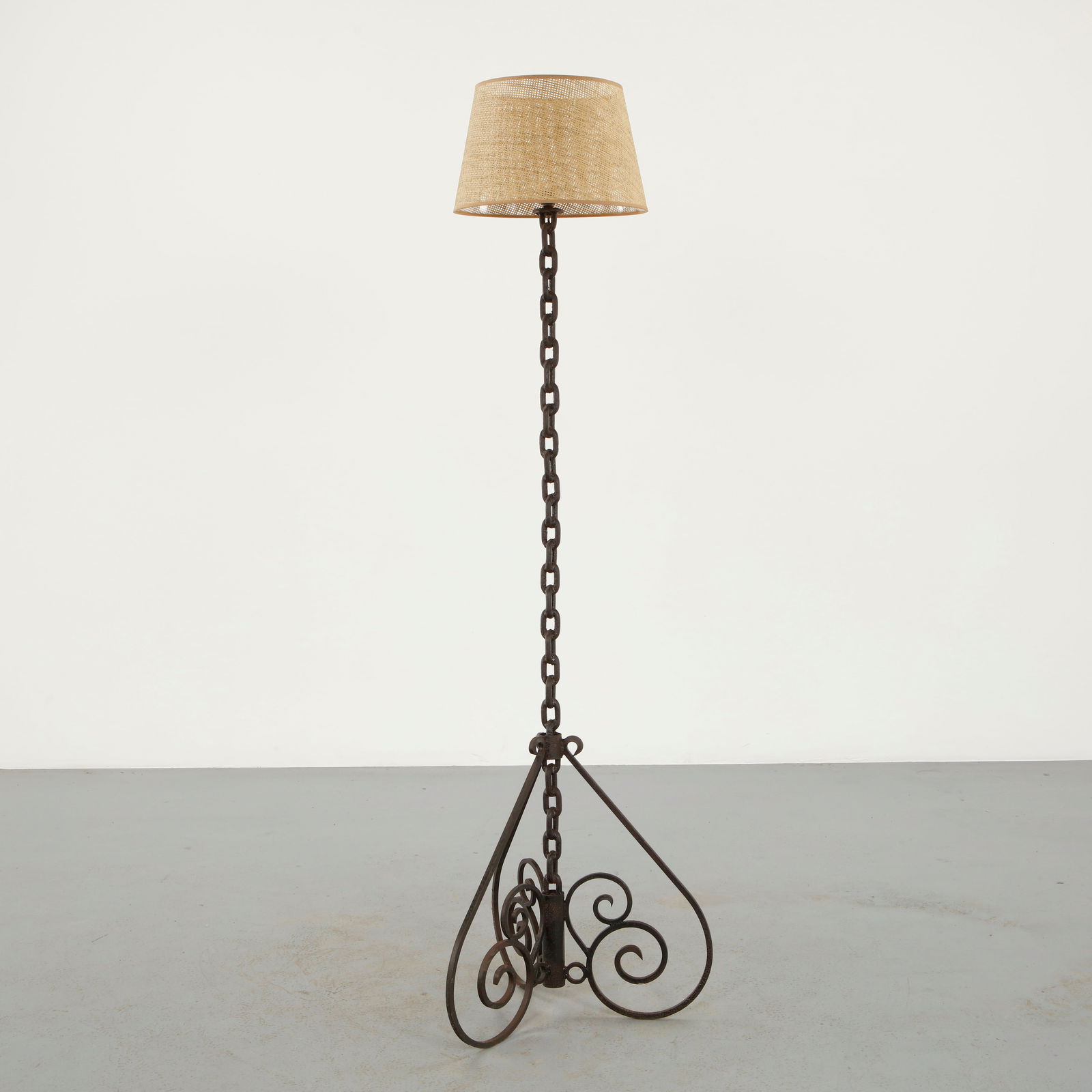 Metal Floor Lamp in the style of Jean Royer, 1950s: Constructed from forged metal with a decorative scrolled base and a vertical chain column, the lamp reflects the expressive ironwork associated with mid-century European craftsmanship. The sculptural