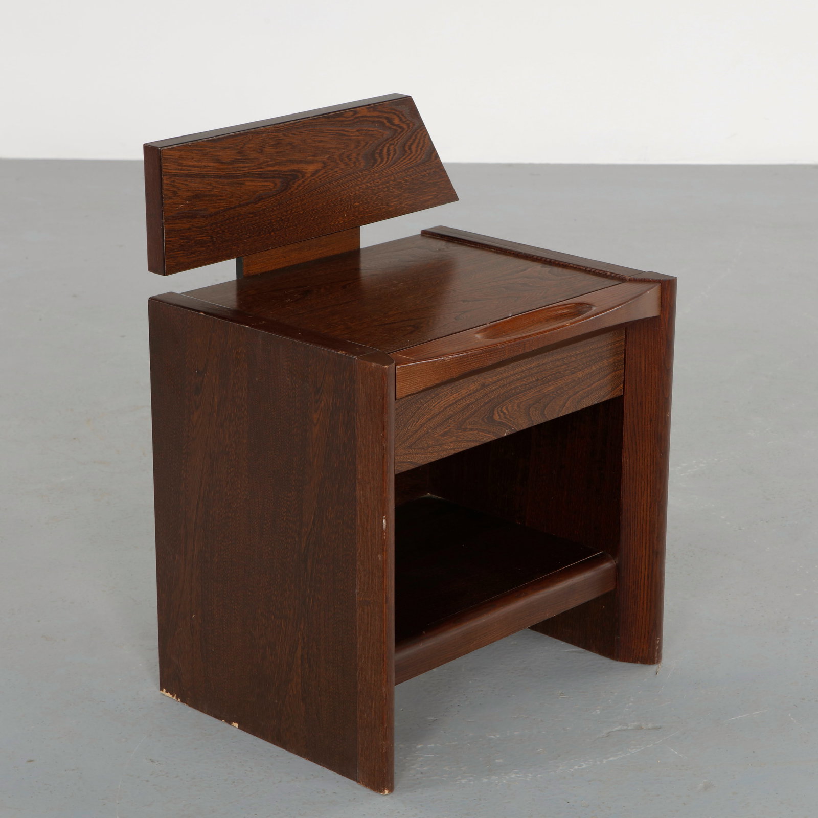 Brutalist Pine Nightstand, 1970s: Constructed in solid pine with a compact architectural silhouette featuring a raised back and open storage shelf. The bold geometry and pronounced grain highlight the rustic modern character of the pi