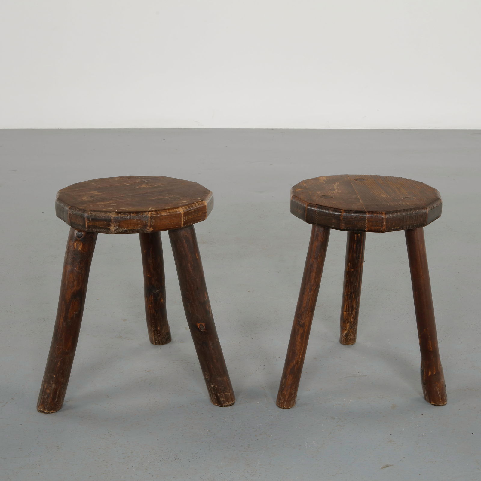 Pair of Rustic Tripod Stools, 1960s: Crafted in solid wood with thick circular seats supported by splayed cylindrical legs. The weathered surfaces and honest construction convey the character of traditional rural craftsmanship. Heig
