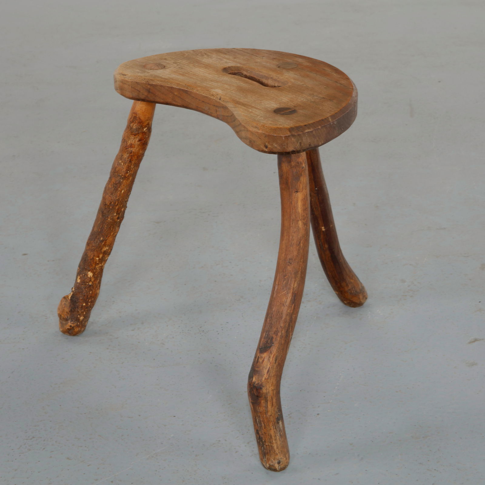 Brutalist Crescent Seat Stool, 1960s: Solid wood stool featuring a thick half moon shaped seat raised on three sturdy cylindrical legs. The expressive grain and hand shaped contours highlight its sculptural presence and raw brutalist mate