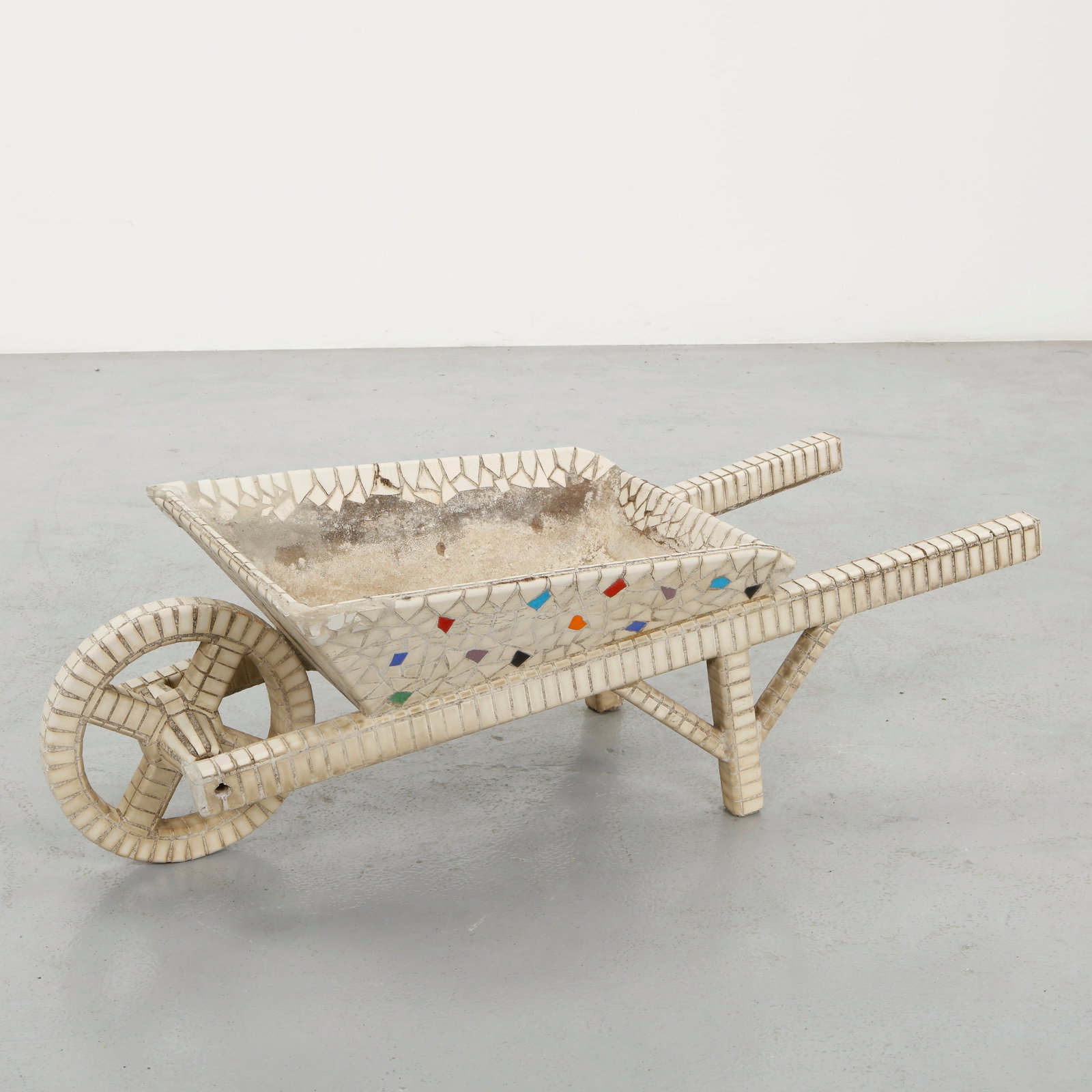 Mosaic Tile Wheelbarrow, 1960s: A charming and unusual decorative wheelbarrow entirely clad in hand-laid mosaic, featuring a faceted basin with subtle polychrome accents. The structure, including the wheel and handles, is meticulous