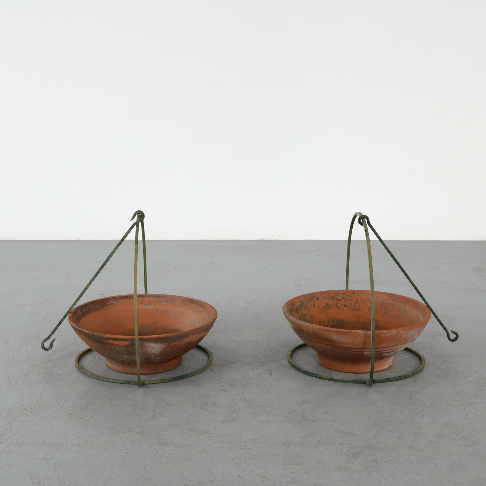 De Roma, Pair of Suspended Terracotta Planters, 1950s: Pair of terracotta planters suspended within metal ring supports, combining functional design with elegant simplicity. The contrast of warm clay and oxidized metal enhances their visual appeal. Height