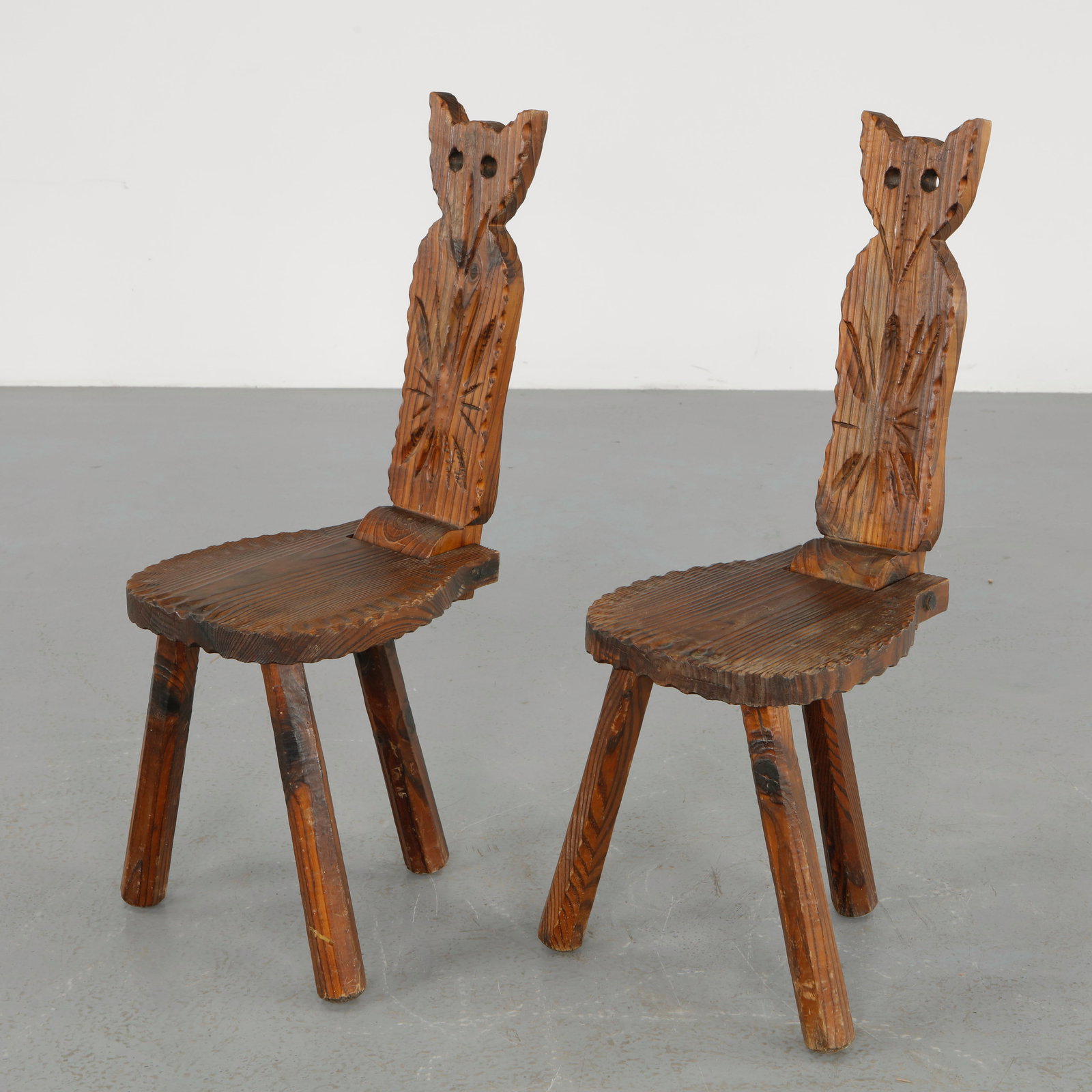 Pair of Brutalist Folding Cat Chairs, 1960s: Pair of folding chairs in carved solid wood featuring stylized feline form backrests with pierced eyes and incised decoration. Their sculptural silhouette and expressive hand carved surface reflect a