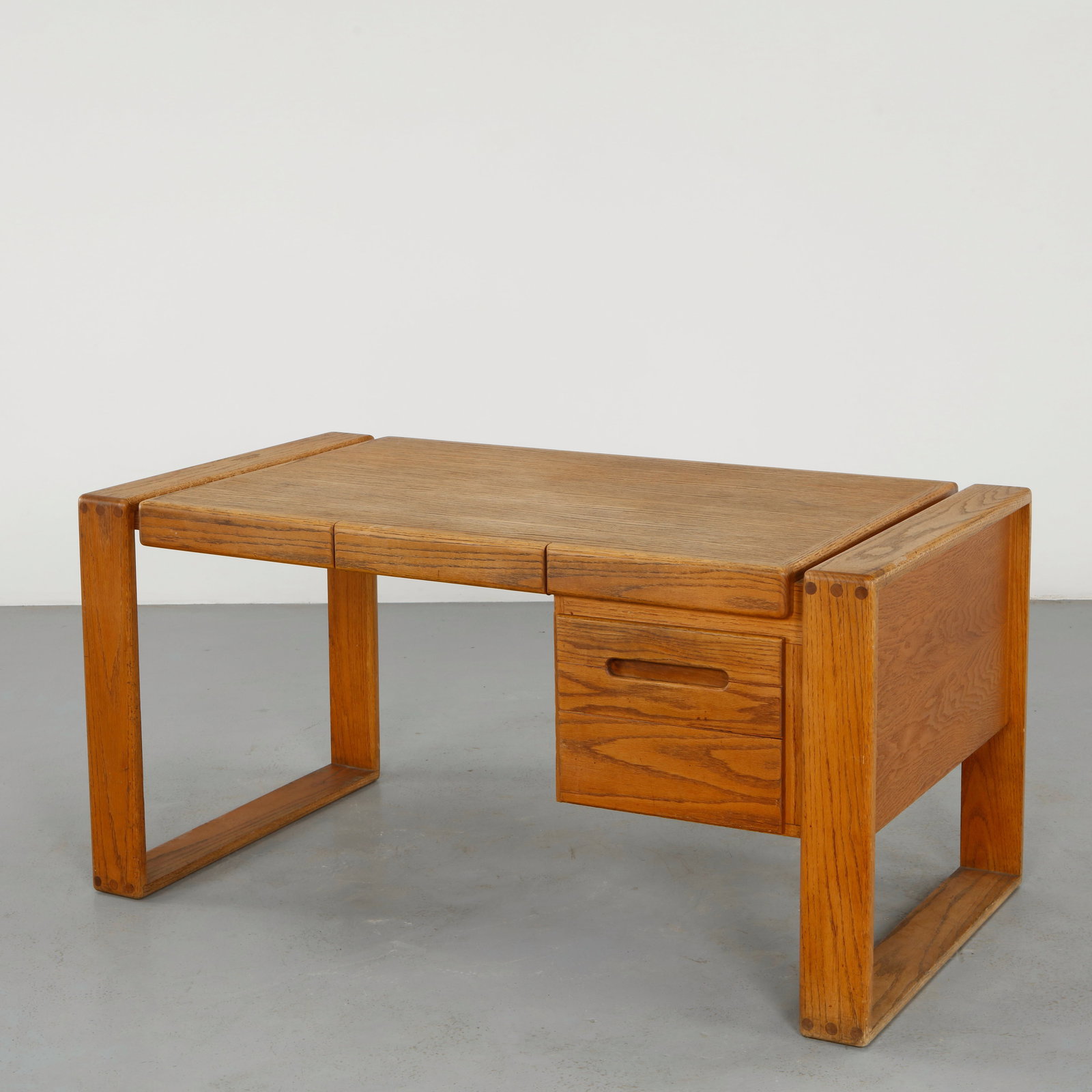 Lou Hodges for California Design Group, Handcrafted Solid Oak Desk, 1979: Signed and stamped. A beautifully crafted desk in solid oak, featuring a distinctive architectural base and integrated drawer with sculpted pull. The warm tone of the wood and precise joinery reflect