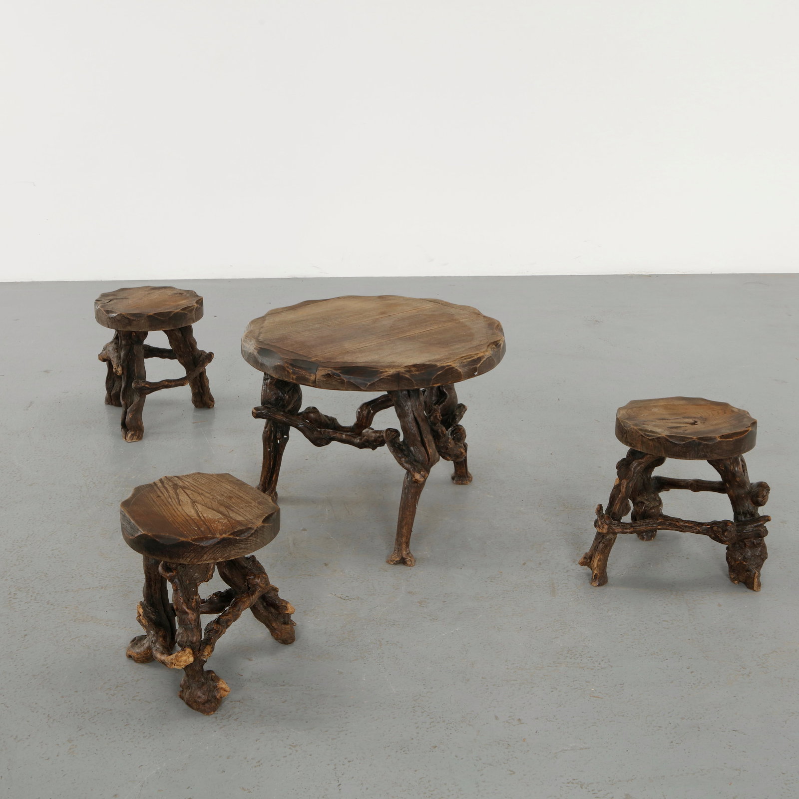French Workshop, Set of Vine Stools and Coffee Table, 1950s: Set composed of a central table and accompanying stools carved from solid vine wood, emphasizing natural forms and textures. The irregular edges and organic bases evoke a sculptural, almost primitive