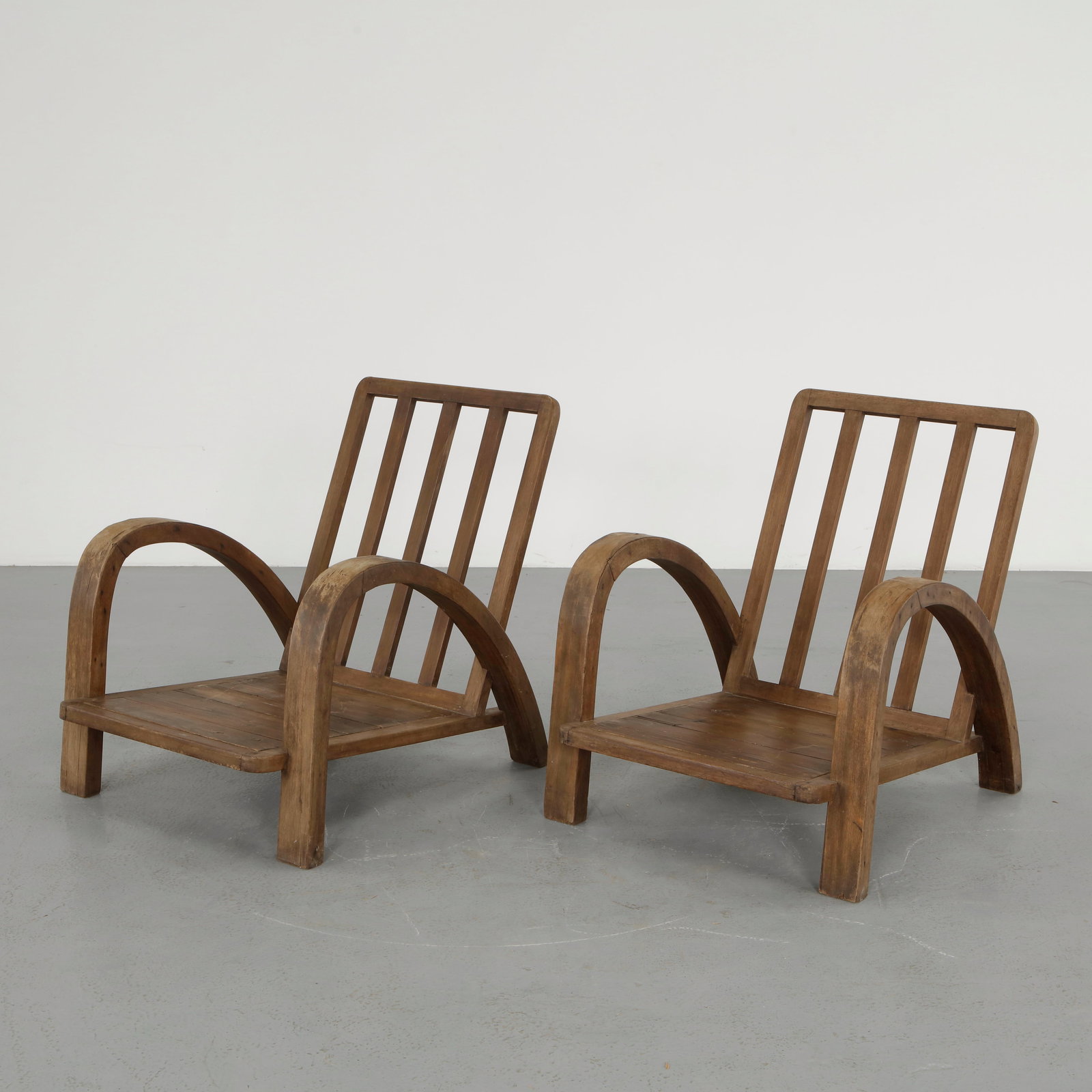 Pair of French Lounge Chairs attributed to Francis Jourdain, 1930s: Pair of lounge chairs executed in solid wood, featuring bold curved armrests and a slatted backrest. The robust construction and expressive forms highlight a vernacular approach to design. A striking