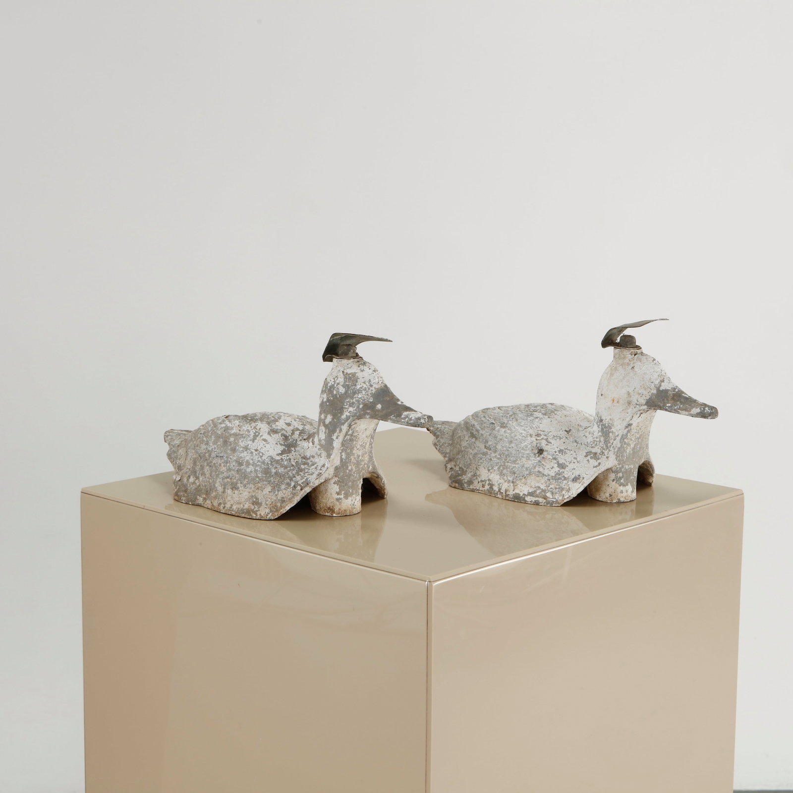 Pair of Concrete Duck Sculptures, 1960s: Pair of reclining duck sculptures in cast concrete with elongated forms and weathered surfaces, each surmounted by a small metal crest. A charming and unusual decorative pair, well suited to a garden
