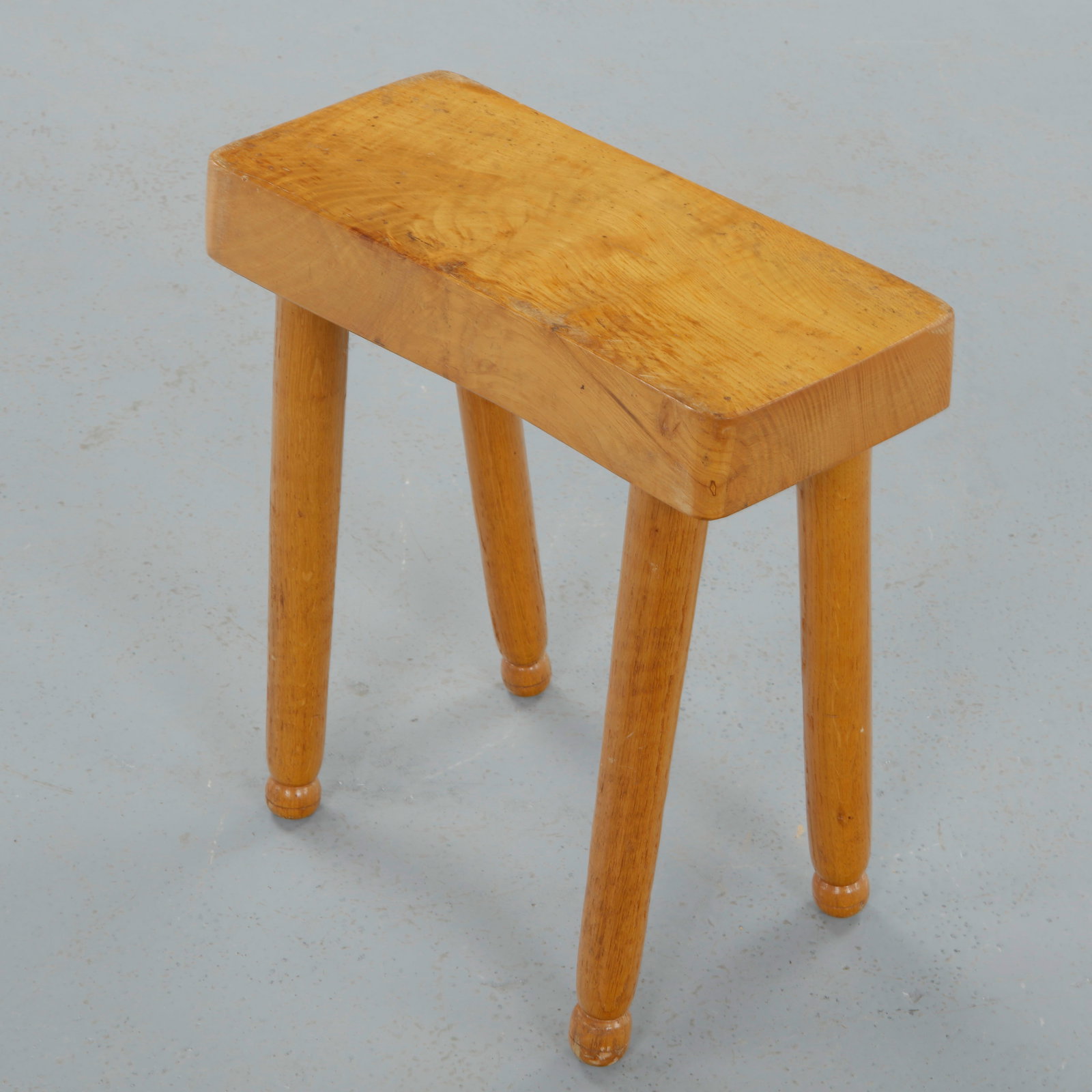 French Provincial Rectangular Rustic Bench Stool, 1950s: Executed in solid wood with a thick rectangular seat and straight cylindrical legs, this low stool reflects utilitarian clarity and robust joinery. The hand finished surface and balanced proportions e
