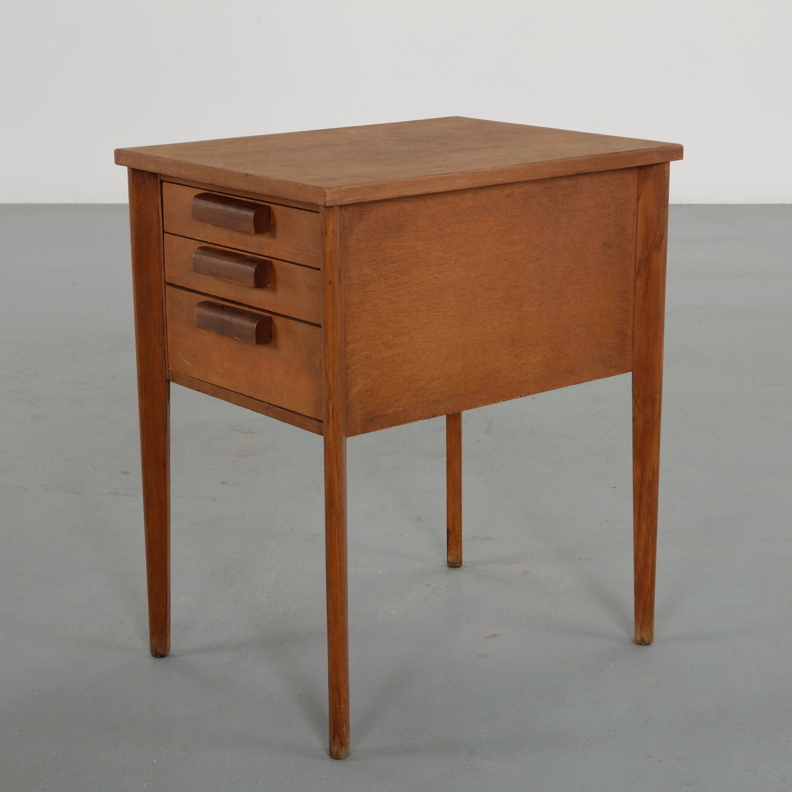 Scandinavian Three-Drawer Nightstand, 1960s: Executed in warm toned wood and raised on slender tapered legs. The three drawers feature sculpted wooden pulls reflecting the restrained elegance and functional clarity of Scandinavian modern design.