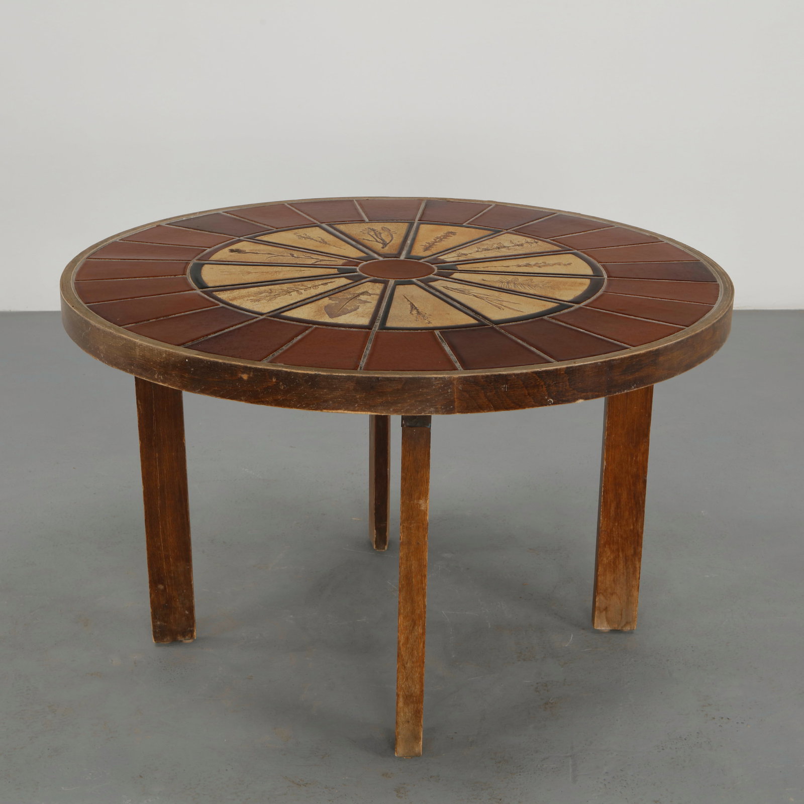 Roger Capron, Round Ceramic Dining Table, 1960s: A beautifully and extrermely rare round dining table featuring a ceramic tile top decorated with stylized botanical motifs arranged in a radial composition. The warm earthy tones contrast elegantly wi