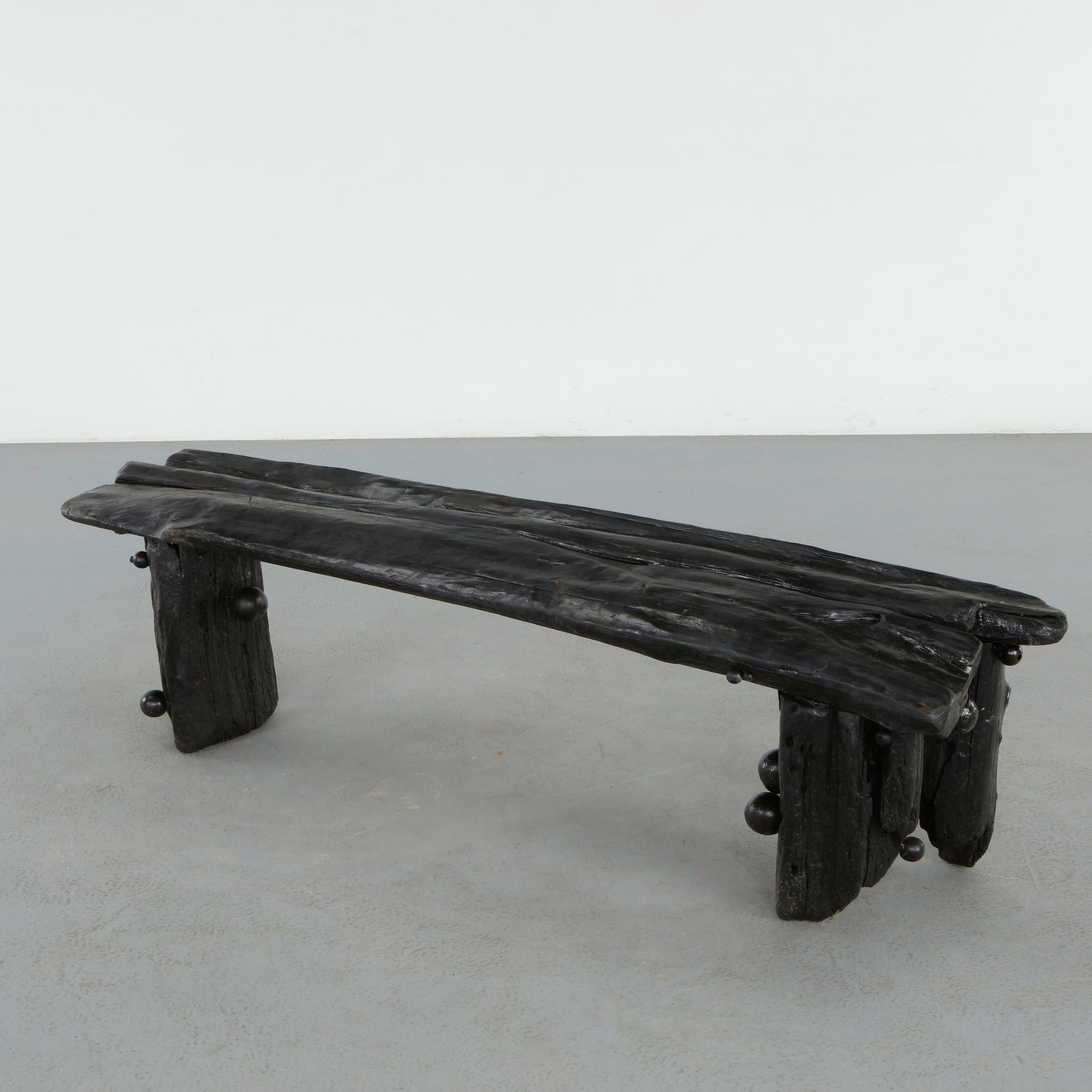 Brutalist Bench in the style of Logniture: Sculptural brutalist bench executed in heavily textured carved wood with a dramatic charred finish and monolithic silhouette. The primitive architectural form and expressive craftsmanship evoke the or
