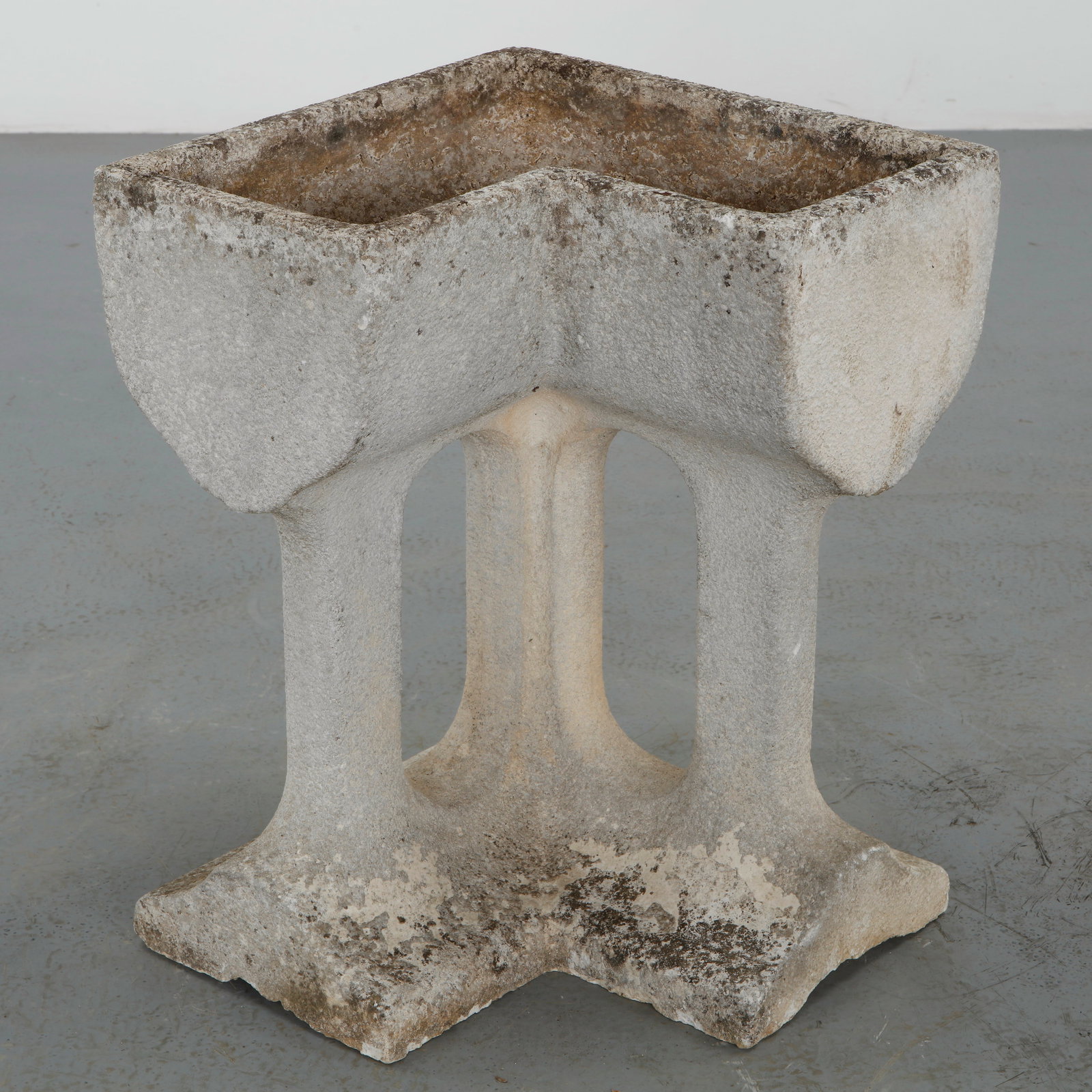 Stone Pillared Corner Planter, 1960s: Sculptural stone corner planter executed with an elevated openwork pedestal and angular basin. The piece displays a richly weathered surface acquired through decades of outdoor exposure, enhancing its