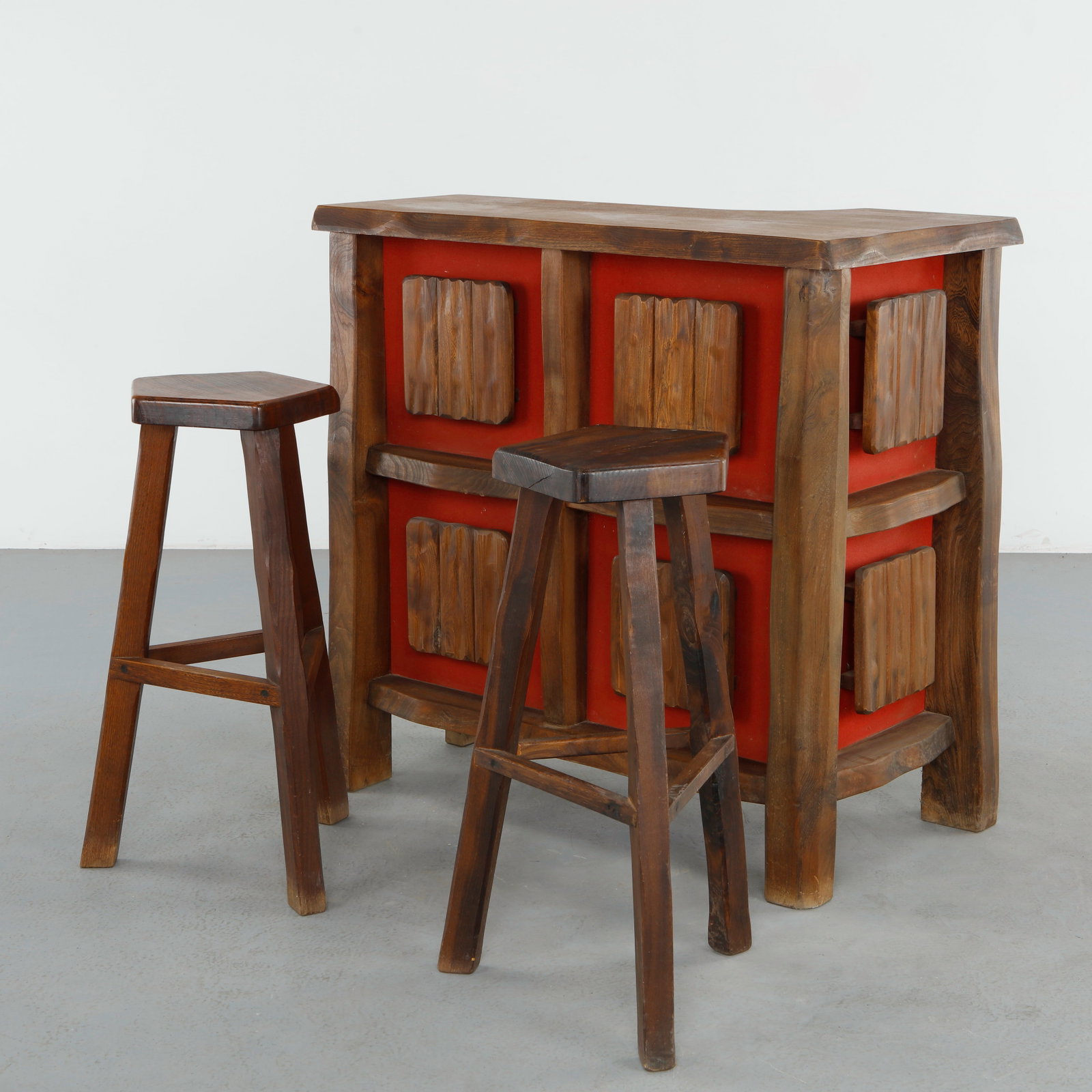 Aramjou, Brutalist Bar Cabinet in Wood with Matching Stools, 1960s: Sculptural Brutalist bar cabinet crafted in richly grained wood with bold geometric carvings set against vivid red lacquered panels. The integrated recessed lighting concealed within the carved wooden