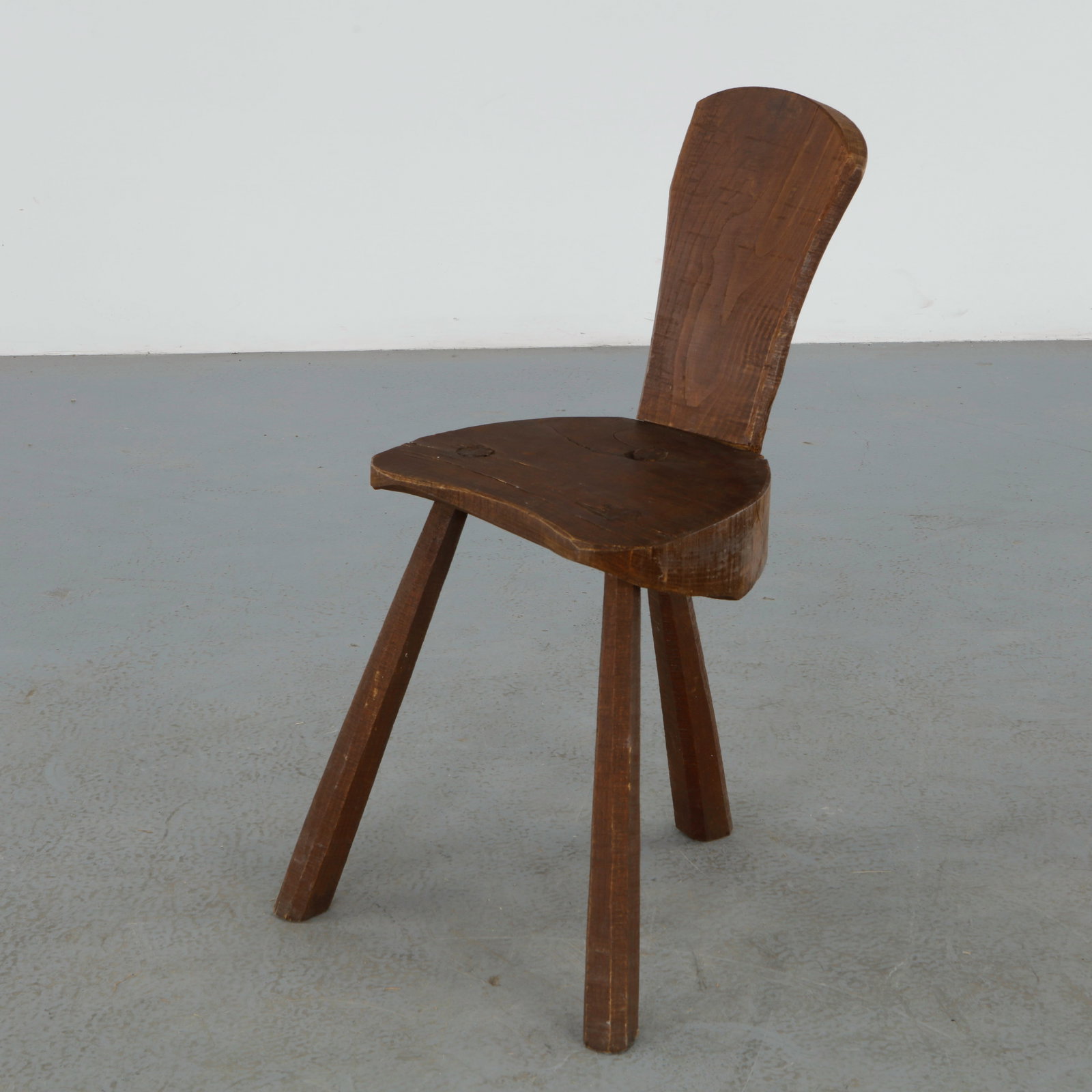 Brutalist Tripod Chair, 1950s: Crafted from thick solid wood with a hand hewn surface, this sculptural tripod chair features an organic silhouette and expressive grain throughout. A striking example of rustic brutalist craftsmanshi