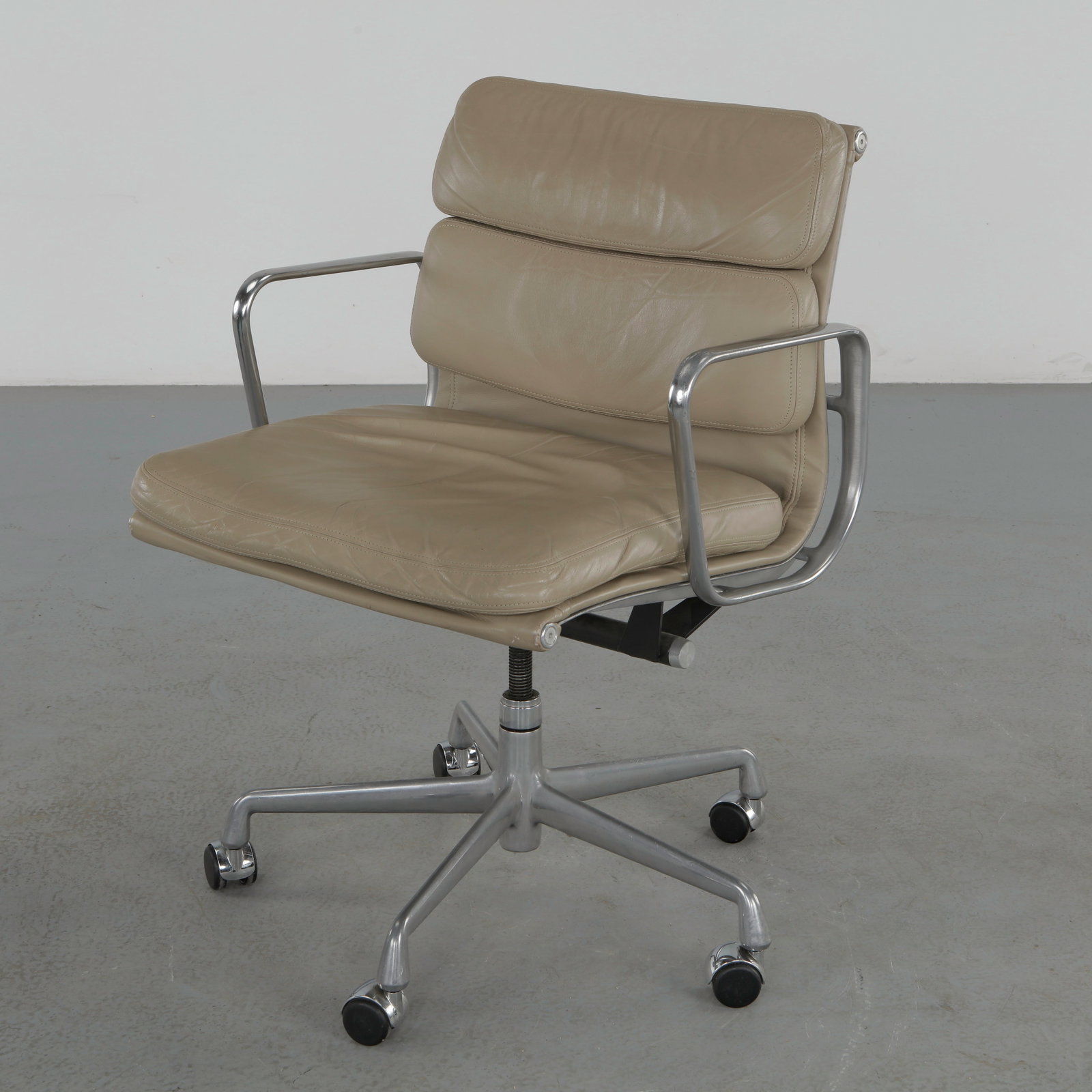Herman Miller Eames Soft Pad Management Chair in Greige Leather: Featuring padded leather cushions mounted on an aluminum frame with a swivel base on casters. A timeless office chair combining ergonomic comfort with refined modernist design. Height: 35.5 in. Width: