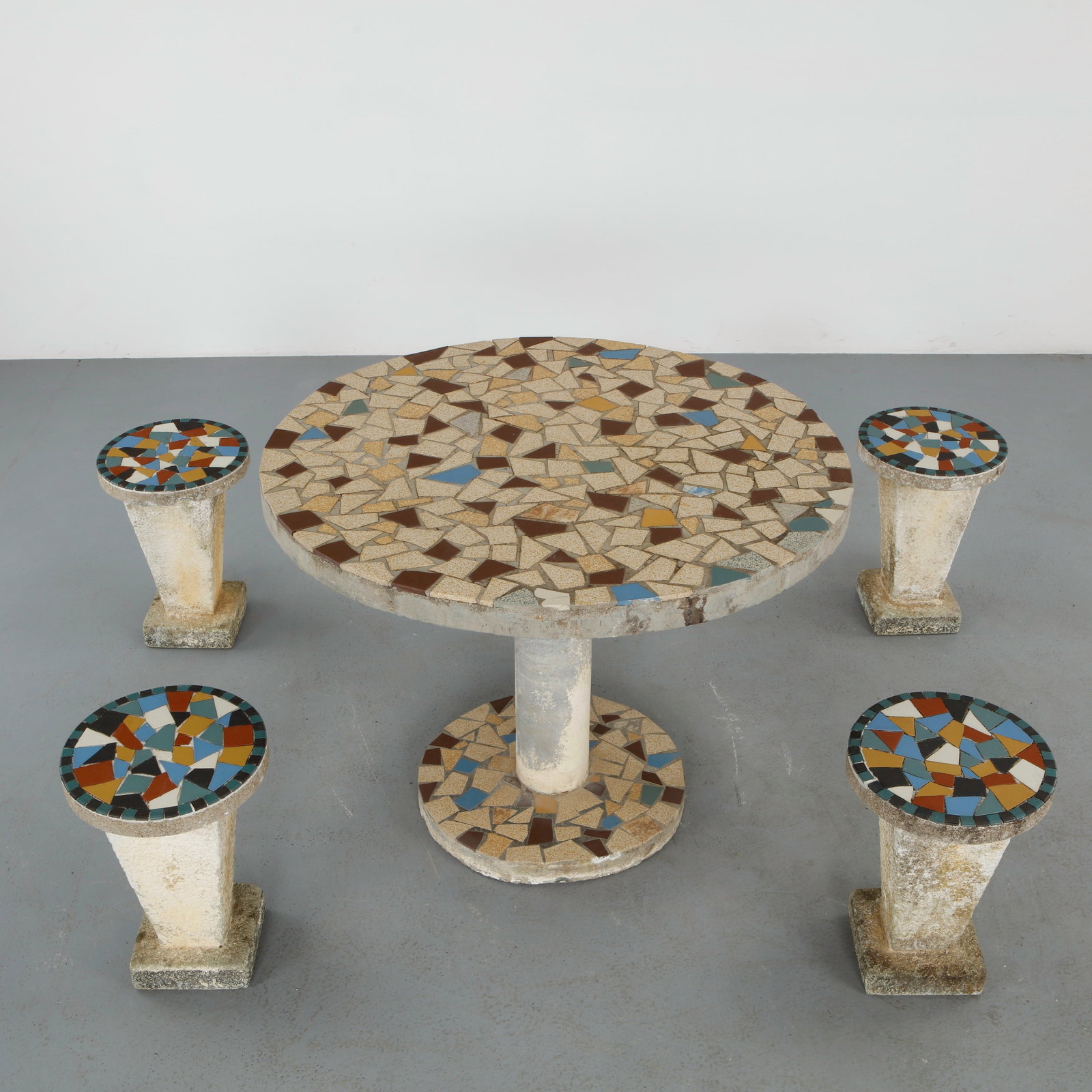 Multicolor Mosaic Dining Set, 1960s: A cohesive outdoor dining ensemble featuring a circular table and four matching stools, each adorned with hand laid mosaic tile surfaces. The composition showcases a refined interplay of color and tex