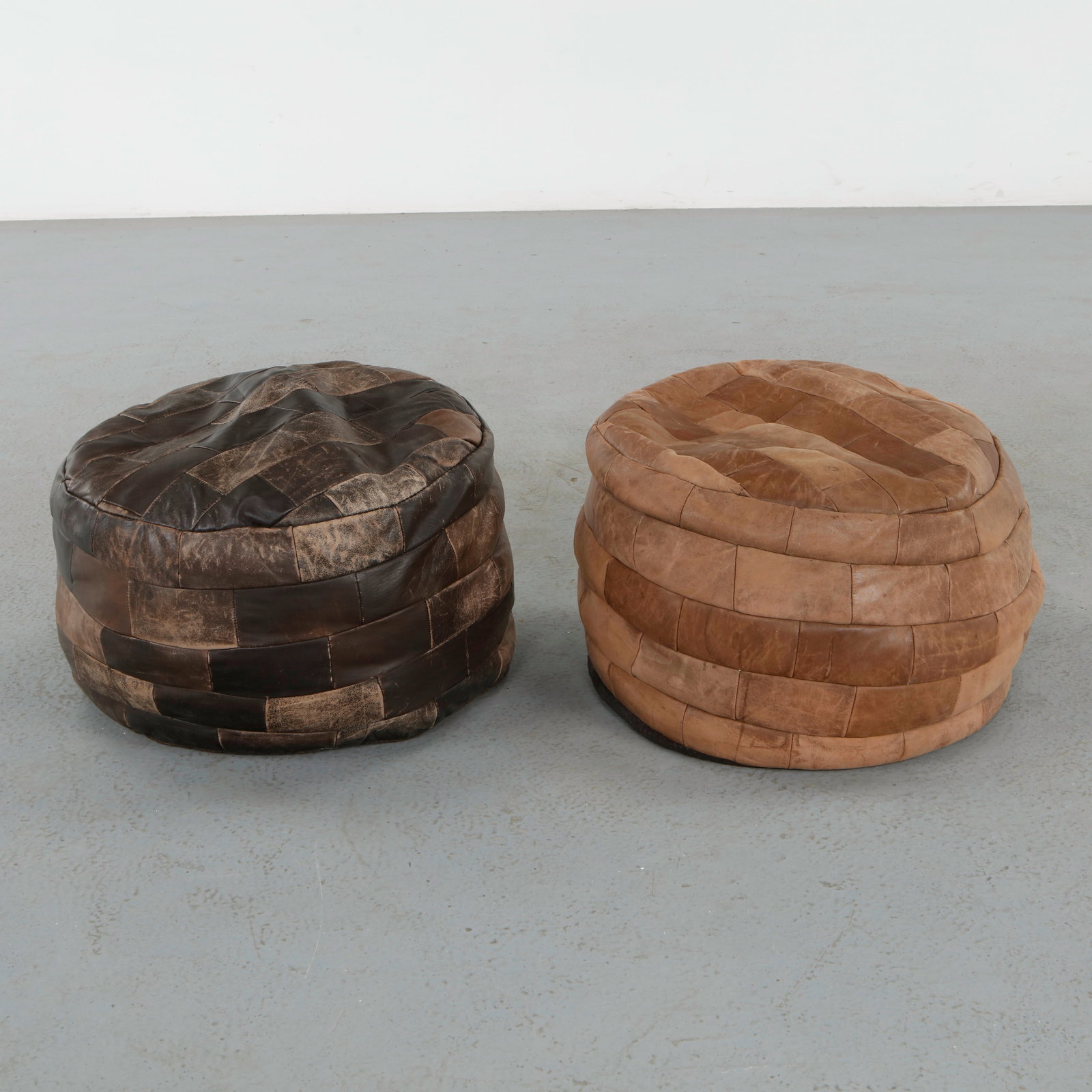 De Sede, Pair of Leather Ottomans, 1960s: Executed in hand-stitched patchwork leather, these sculptural ottomans exemplify De Sede signature craftsmanship and supple upholstery. Their brown and camel tones and generous forms invite both comfo
