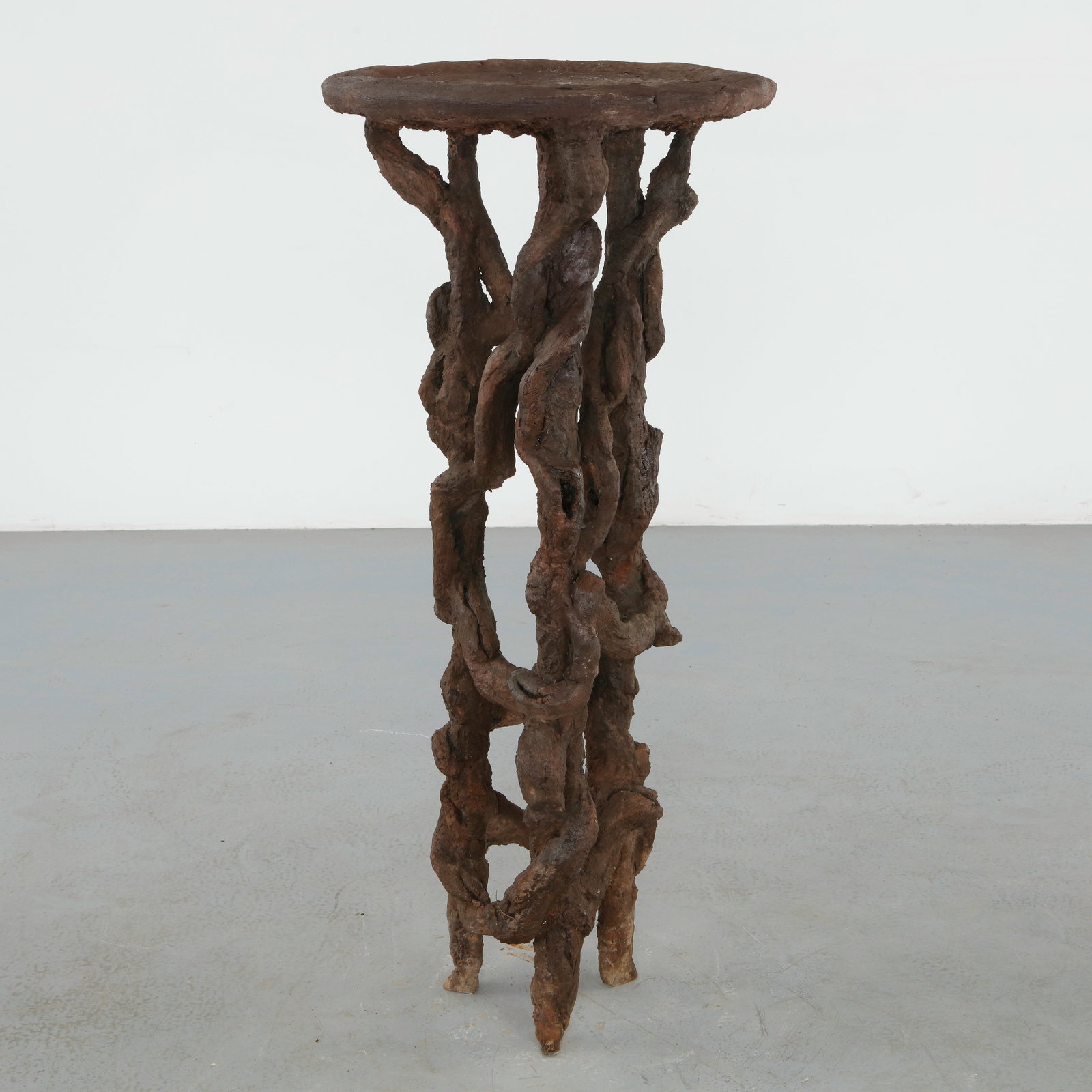 Faux Bois Concrete Pedestal: Sculptural faux bois pedestal executed in hand formed concrete, featuring an intricate arrangement of intertwined branch form supports beneath a circular top. The richly textured surface and organic s