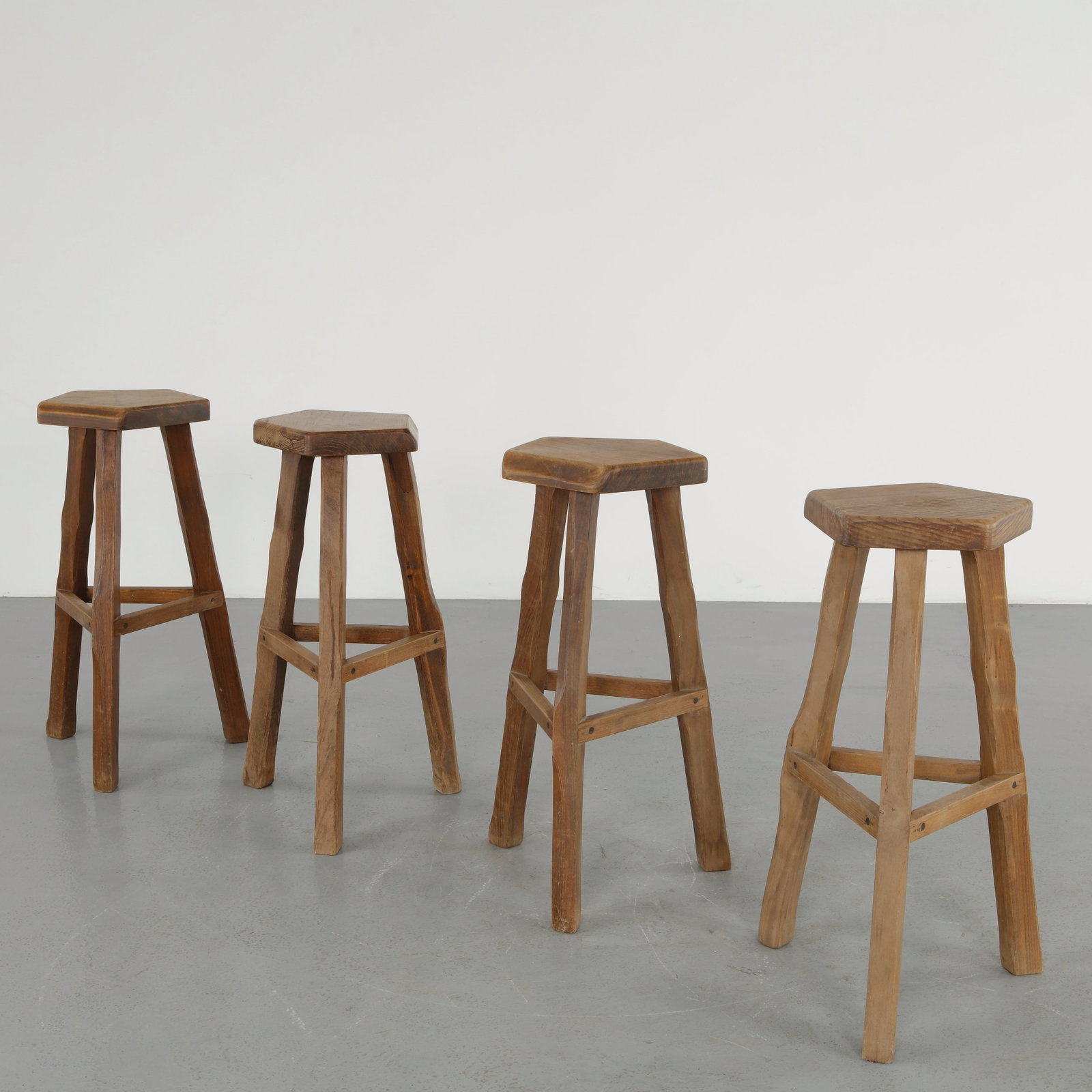 Olavi Hannien, Set of Four Wooden Bar Stools, 1960s: Crafted in solid wood, these bar stools feature thick hexagonal seats raised on robust angular legs joined by stretchers, emphasizing stability and honest construction. The design reflects a rustic mo