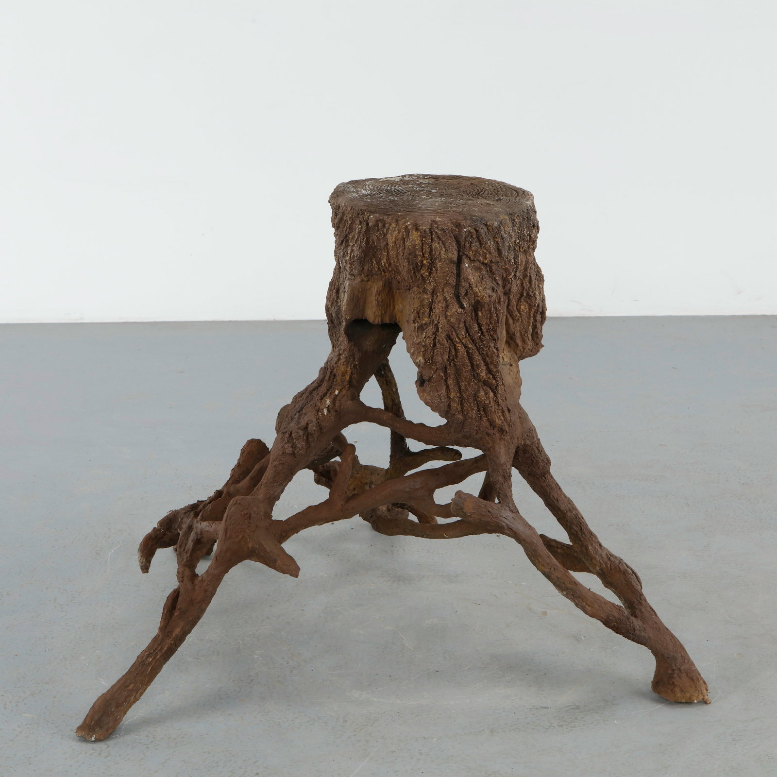 Organic Faux Bois Pedestal: Organic faux bois pedestal featuring an intricate root form base supporting a circular top with simulated wood grain carving. The sculptural silhouette captures the handcrafted romanticism of rustic g