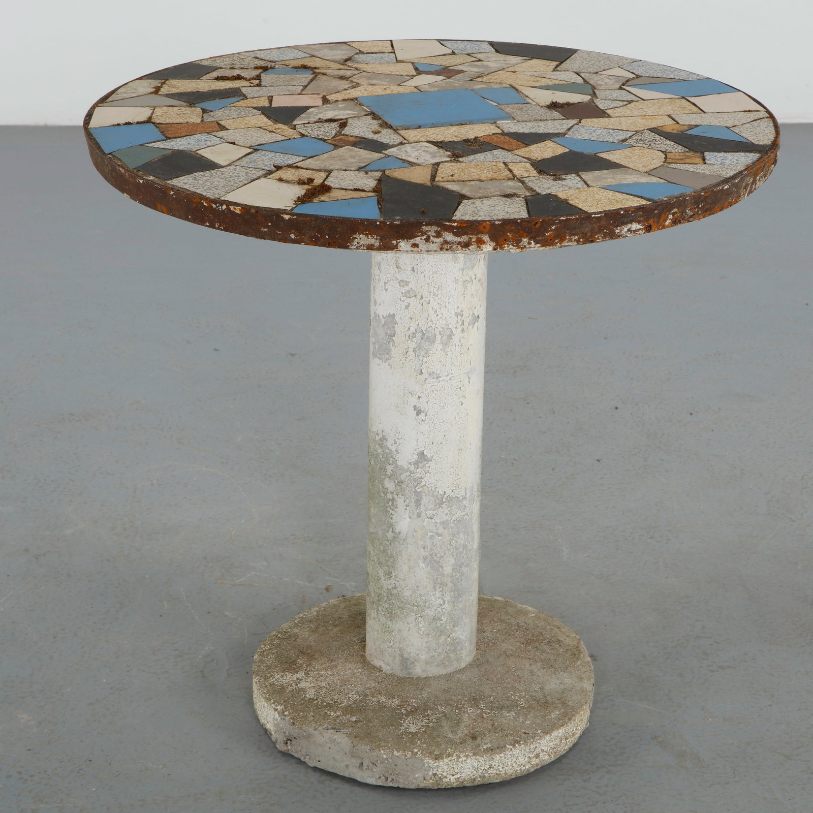 Mosaic Garden Table with Iron Trim, France, 1960s: Circular pedestal table featuring a hand assembled mosaic surface composed of geometric ceramic fragments in soft neutral tones with contrasting blue details. The oxidized iron perimeter and weathered