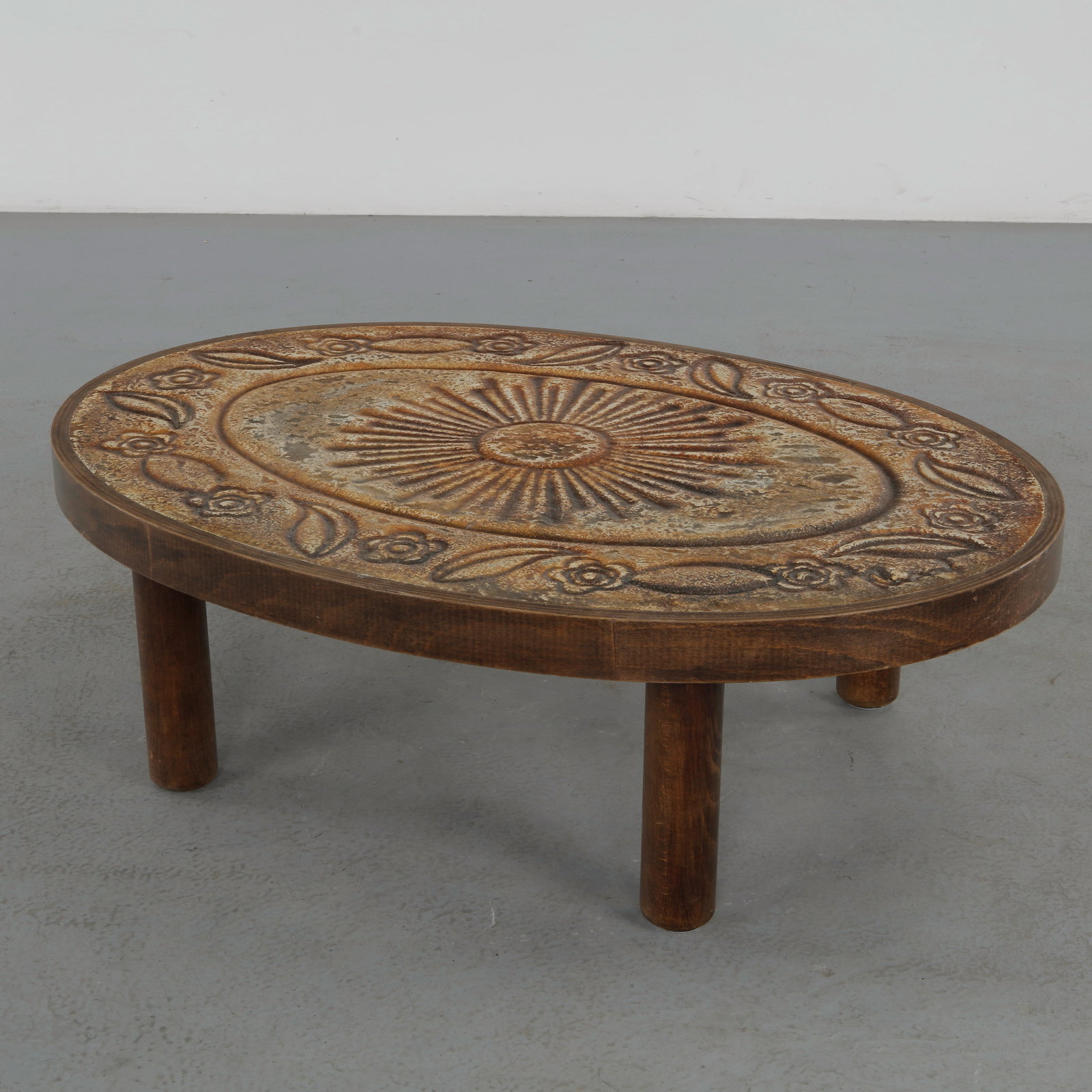Francois Chaty, Ceramic Coffee Table, 1960s: A sculptural French ceramic coffee table featuring a richly textured sunburst motif framed by stylized floral ornamentation. Executed with an earthy glaze palette and raised relief decoration, the pie