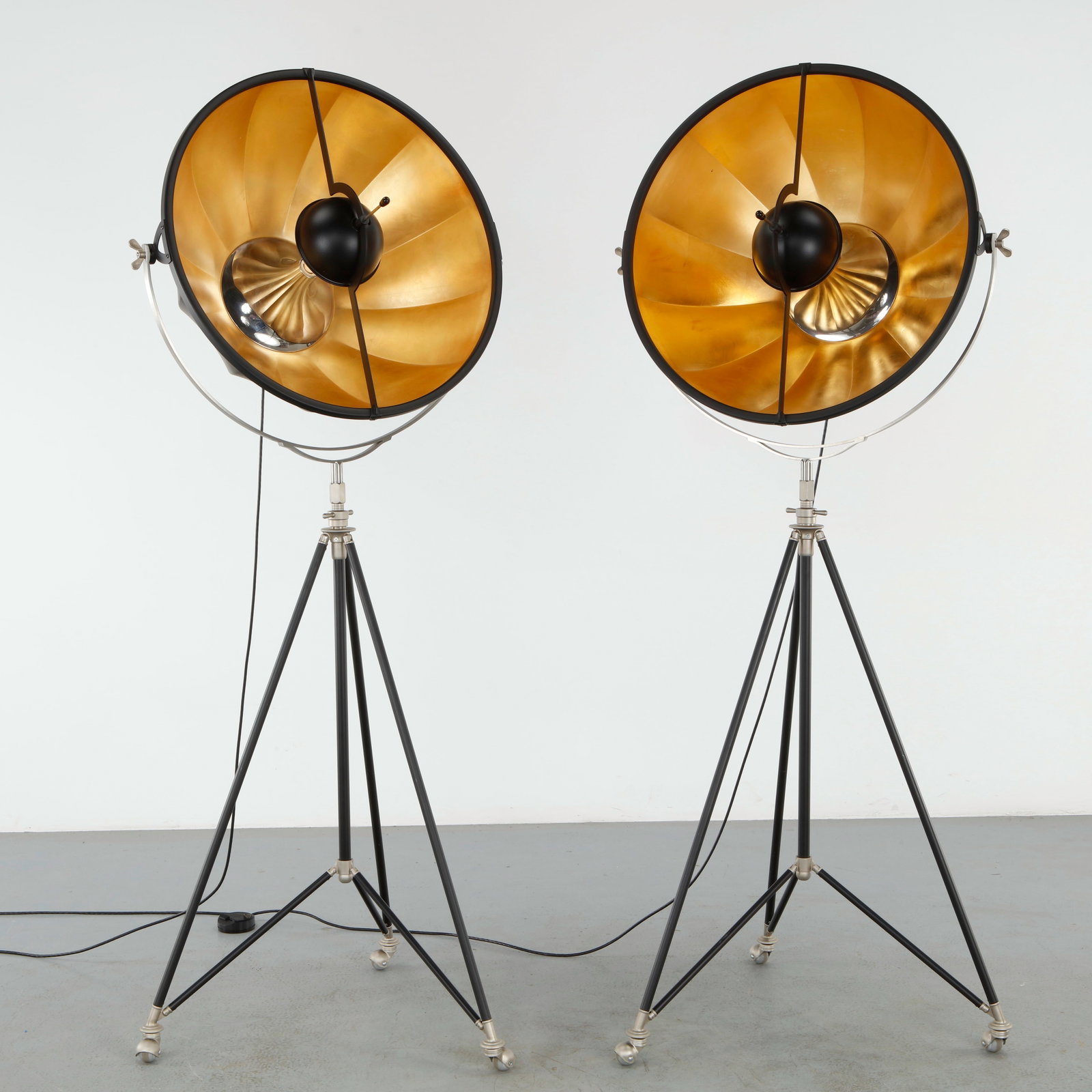 Restoration Hardware, Pair of Fortuny Studio Floor Lamps: Constructed with an adjustable tripod base supporting a large reflector shade with a warm interior finish, inspired by theatrical lighting. A sculptural lighting piece balancing industrial character a